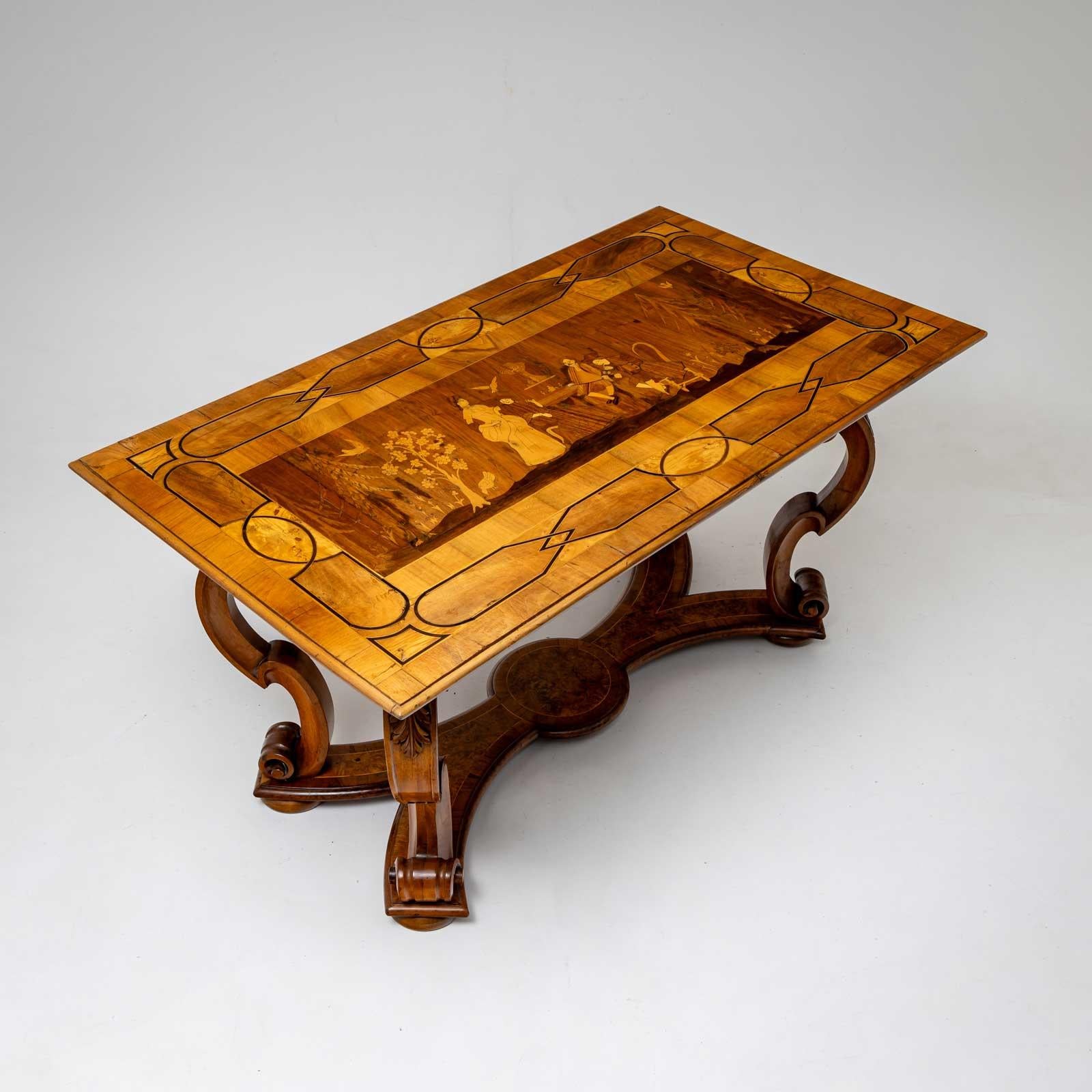 Table de salle à manger en noyer avec des sangles incrustées et une scène figurative incrustée sur le plateau. Les jambes sont incurvées en forme de volute et reliées par une jambe de force en forme de X.