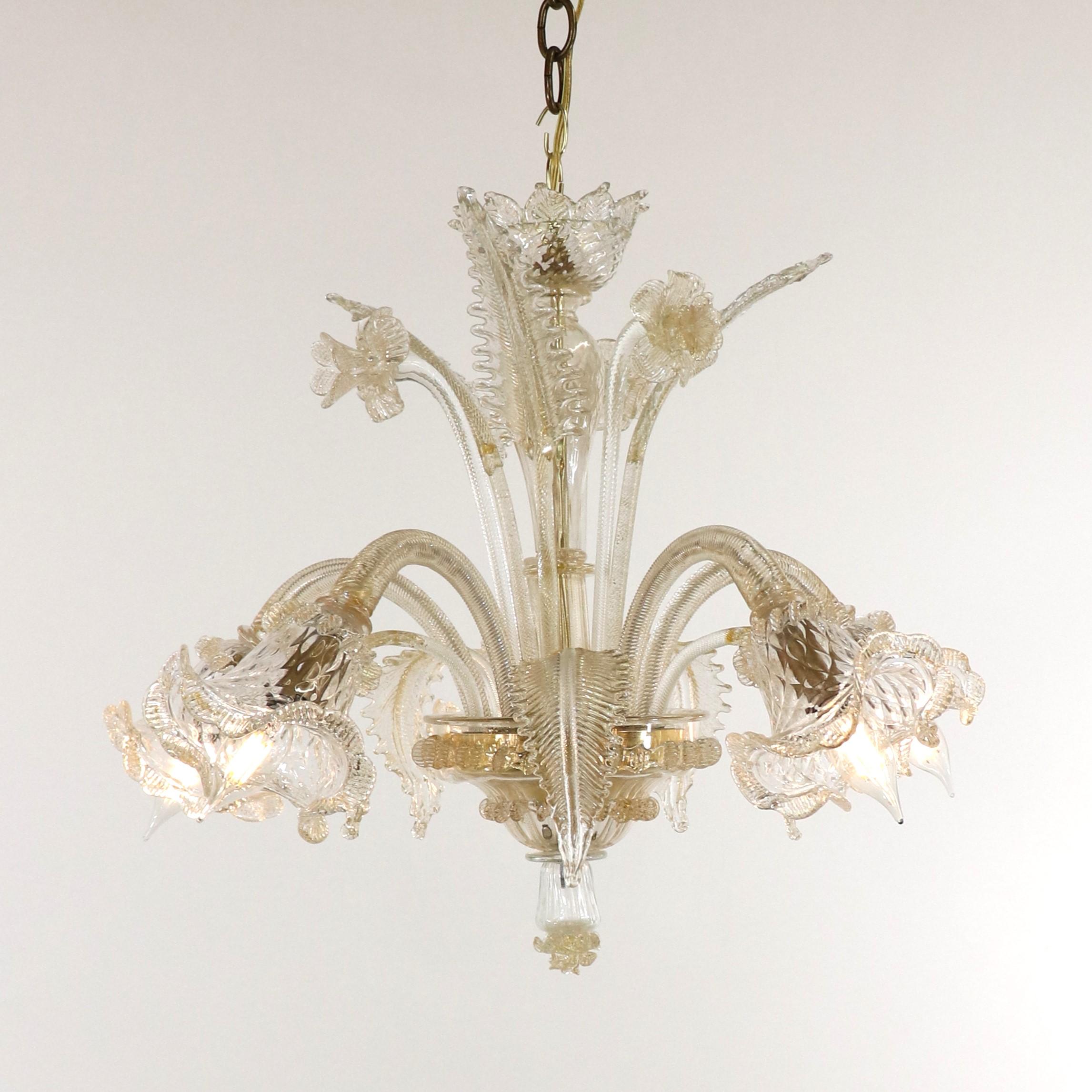 This handcrafted gold-infused cristallo Murano chandelier has five scroll arms with tri-lobed cups, utilizing a rigaree trim. Featuring a bulbous center column with blooming details, stylized here with daffodils and leaves. The glass houses on the