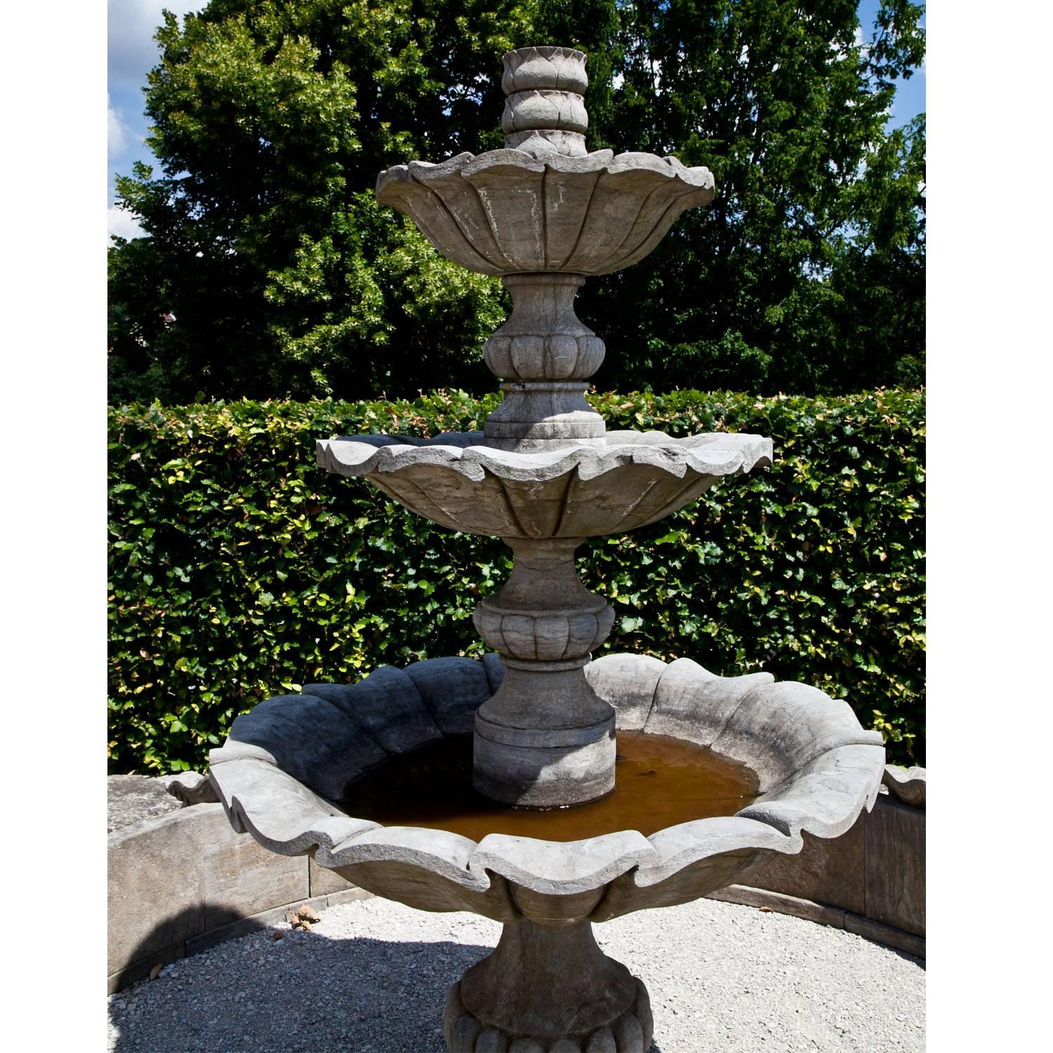Large Baroque-style fountain with a round profiled basin (H: 42cm, Inner dimension: 295cm) and four symmetrically positioned shell-ornaments. The middle column has three tiers and a maximum dimension of 130cm. Each tier stands on a baluster foot and
