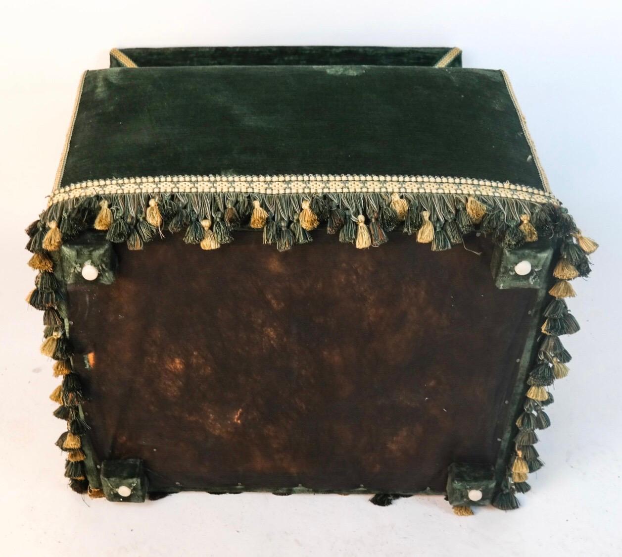 Dog house upholstered with green velvet and green and cream fringe. Hinged top revealing green pillow within.