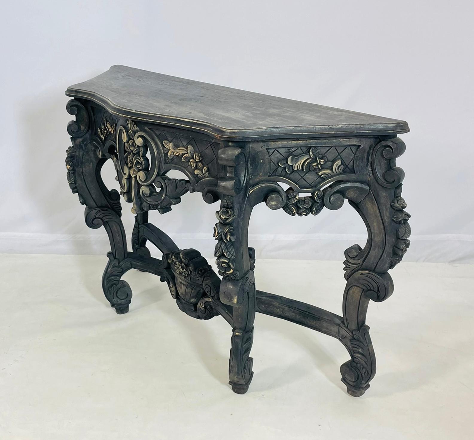 An ornate and richly detailed Baroque-style console table, hand-carved in wood with elaborate scrolling motifs and floral embellishments. This dramatic piece features a shaped top with a distressed, antiqued finish and a robust apron adorned with