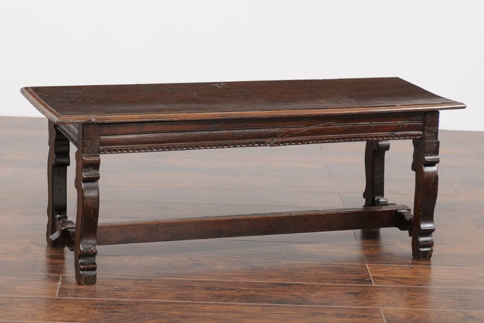 An Italian Baroque style walnut bench from the early 19th century with lyre shaped legs and cross stretcher. This Italian wooden bench features a rectangular single-plank seat with rounded edges, resting above a trestle base with lyre shaped legs,
