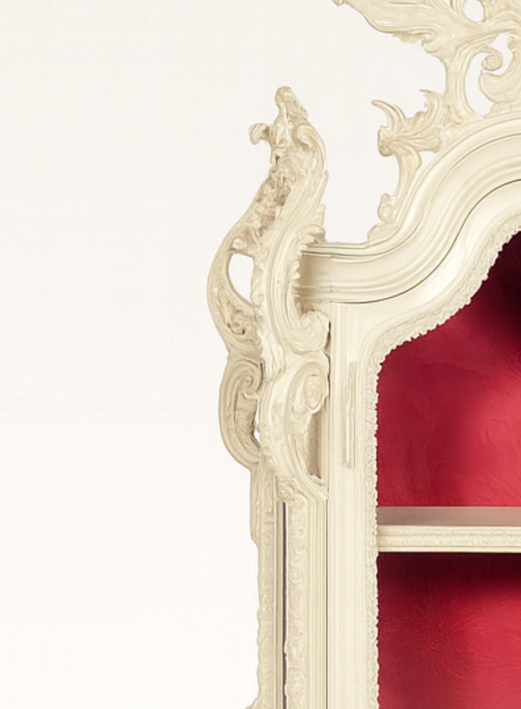 Una rara vitrina de oratorio lacada en blanco roto con  un cuerpo rematado en madera de cedro y nogal ricamente tallada, cabeceras frontal y laterales, puerta acristalada y enmarcada y laterales con recortes curvilíneos en los segmentos superiores.