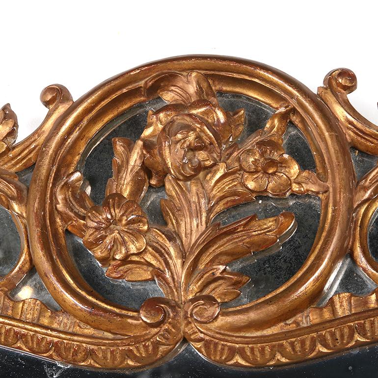 Questo specchio in legno dorato del XIX secolo, in stile barocco, presenta dettagli in acanto sapientemente intagliati che circondano un frontone floreale e un motivo a conchiglia alla base. Uno specchio squisito che sarebbe perfetto sopra un