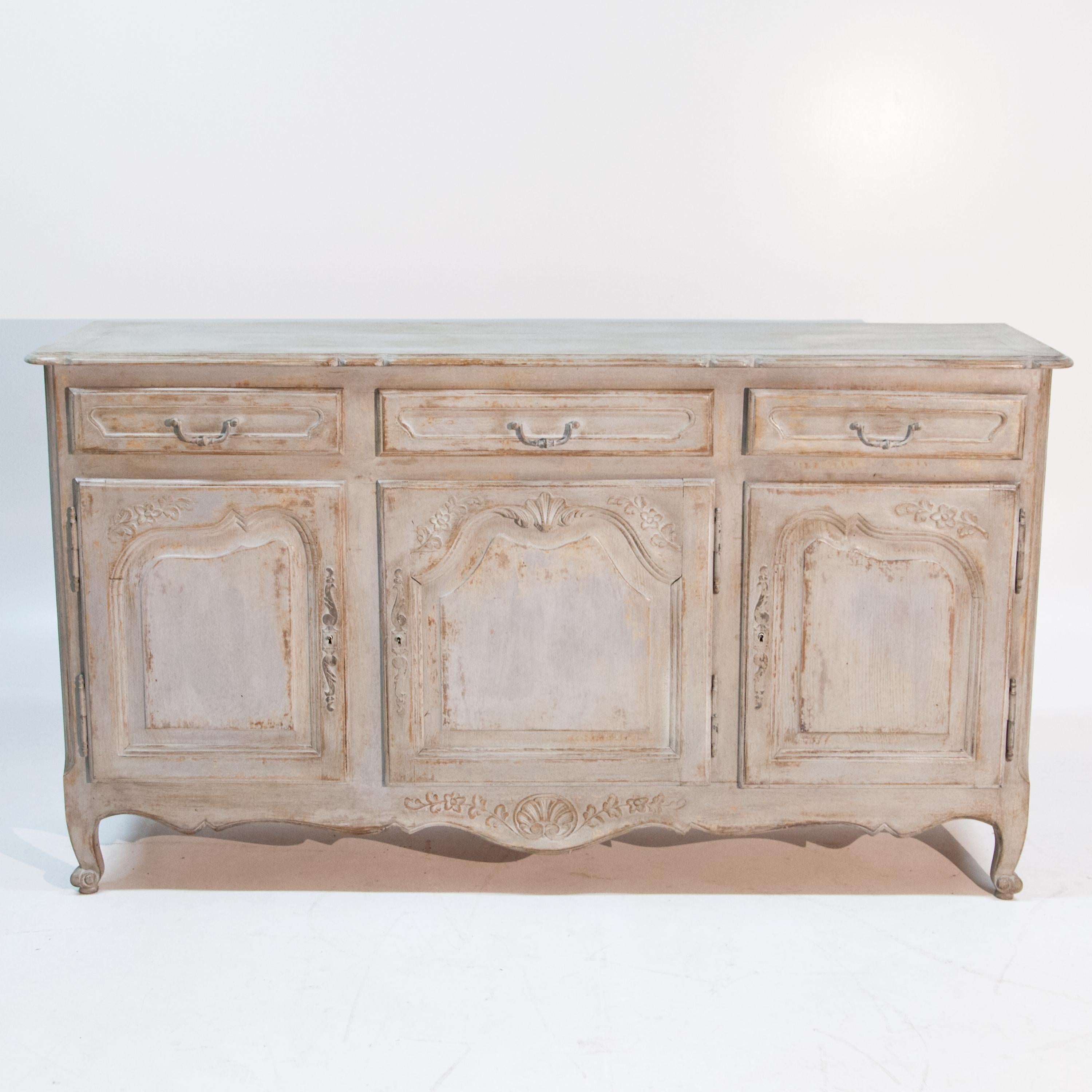 Three-door credenza with three drawers and curved frame, standing on volute feet. The fronts with wavy panels and vine decoration. The grey-beige setting is new and has been decoratively rubbed through.