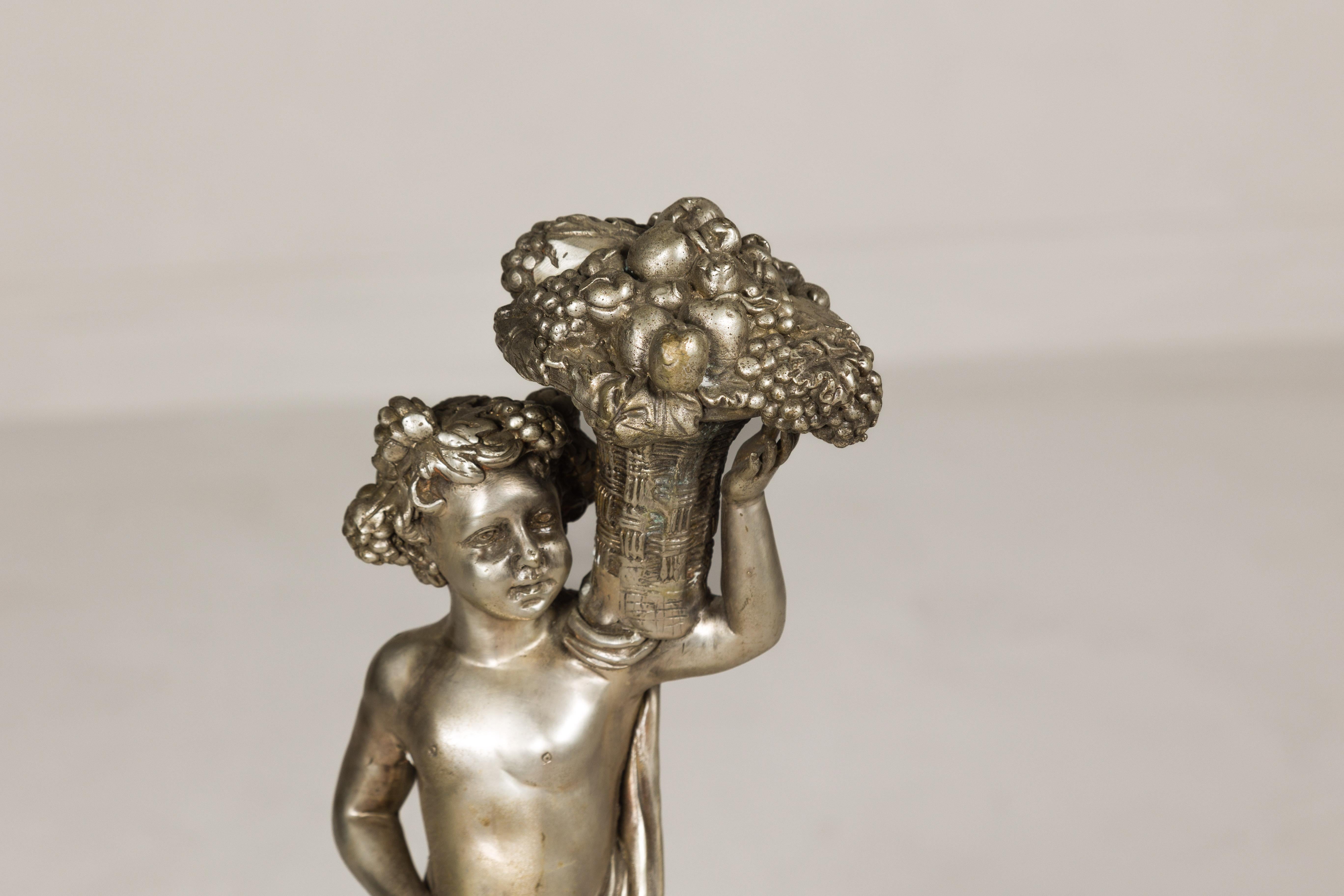 Bronzo Statuetta in bronzo argentato in stile barocco di un putto che porta un cesto di frutta in vendita