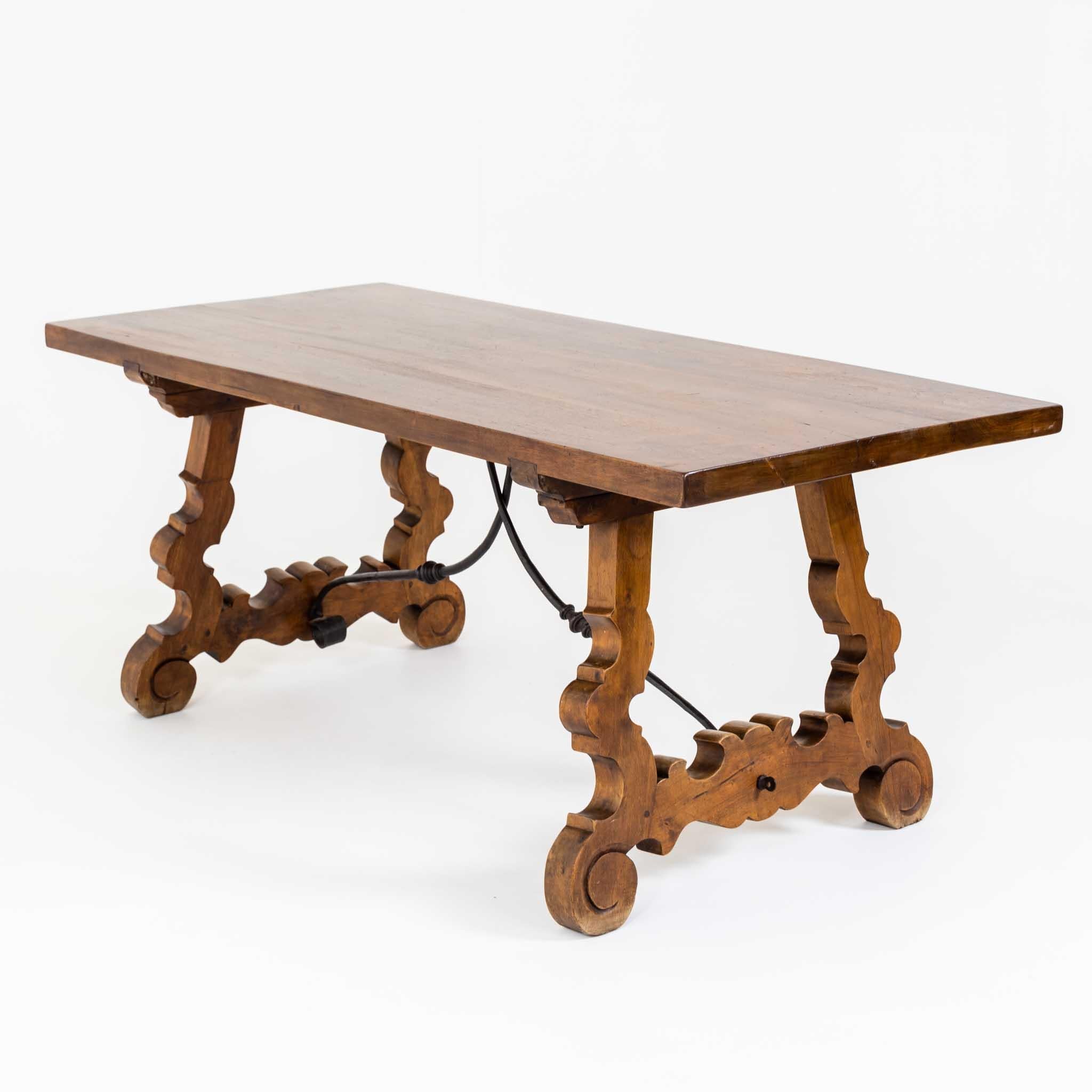 Barocktisch aus massivem Nussbaumholz, mit rechteckiger Tischplatte auf geschwungenen, ausgeschnittenen Beinen und geschwungener Eisenzwischenstrebe.