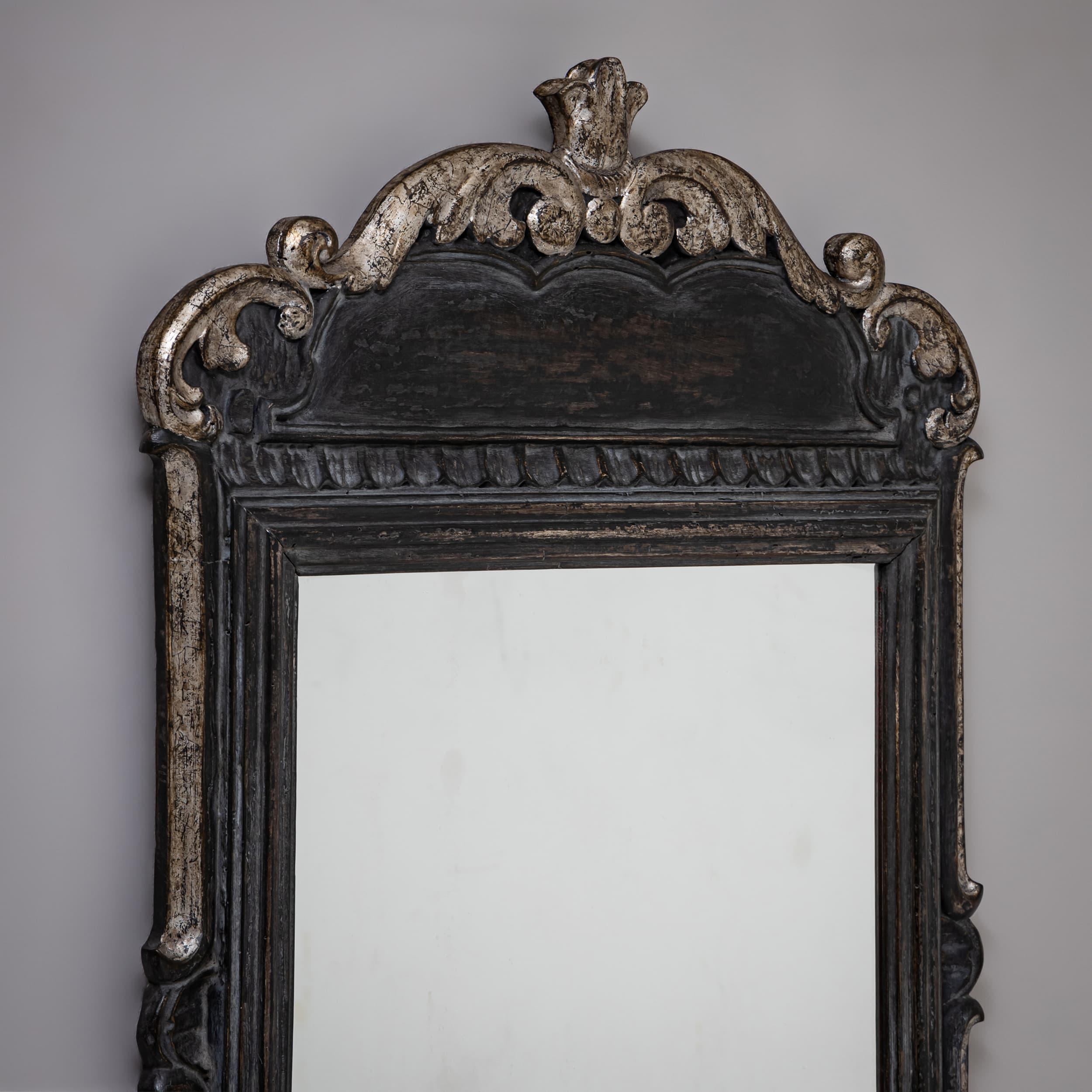 Baroque-style wall mirror with a wooden frame elaborately decorated with rocaille and scroll motifs. The anthracite-gray finish has been newly applied and accented with silver patination along the outer edges.