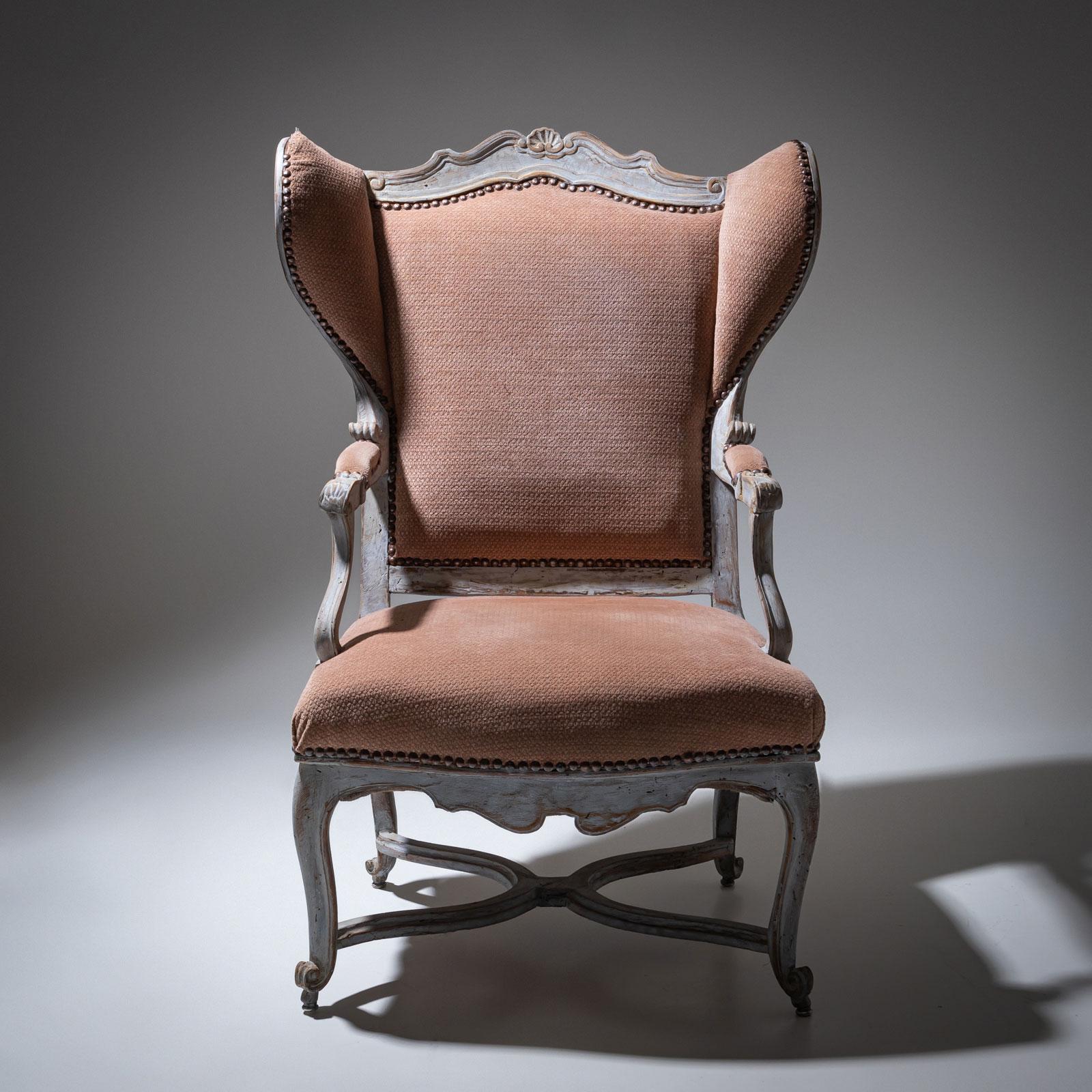 Confortevole sedia wingback in stile barocco, caratterizzata da una struttura graziosamente curva e da decorazioni intricate. Le ali, di dimensioni generose, si inseriscono perfettamente nei braccioli, offrendo un'esperienza di seduta invitante. La