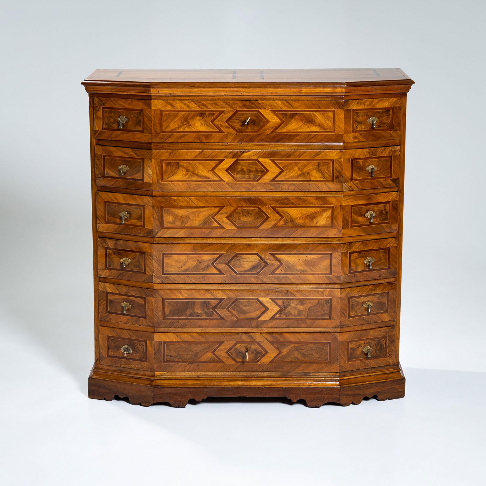 Tall Baroque chest of drawers featuring six drawers with elegant brass knobs. The hexagonal shape is achieved through slightly beveled front corners, giving the piece a distinctive sense of movement. It stands on a gracefully shaped apron and is