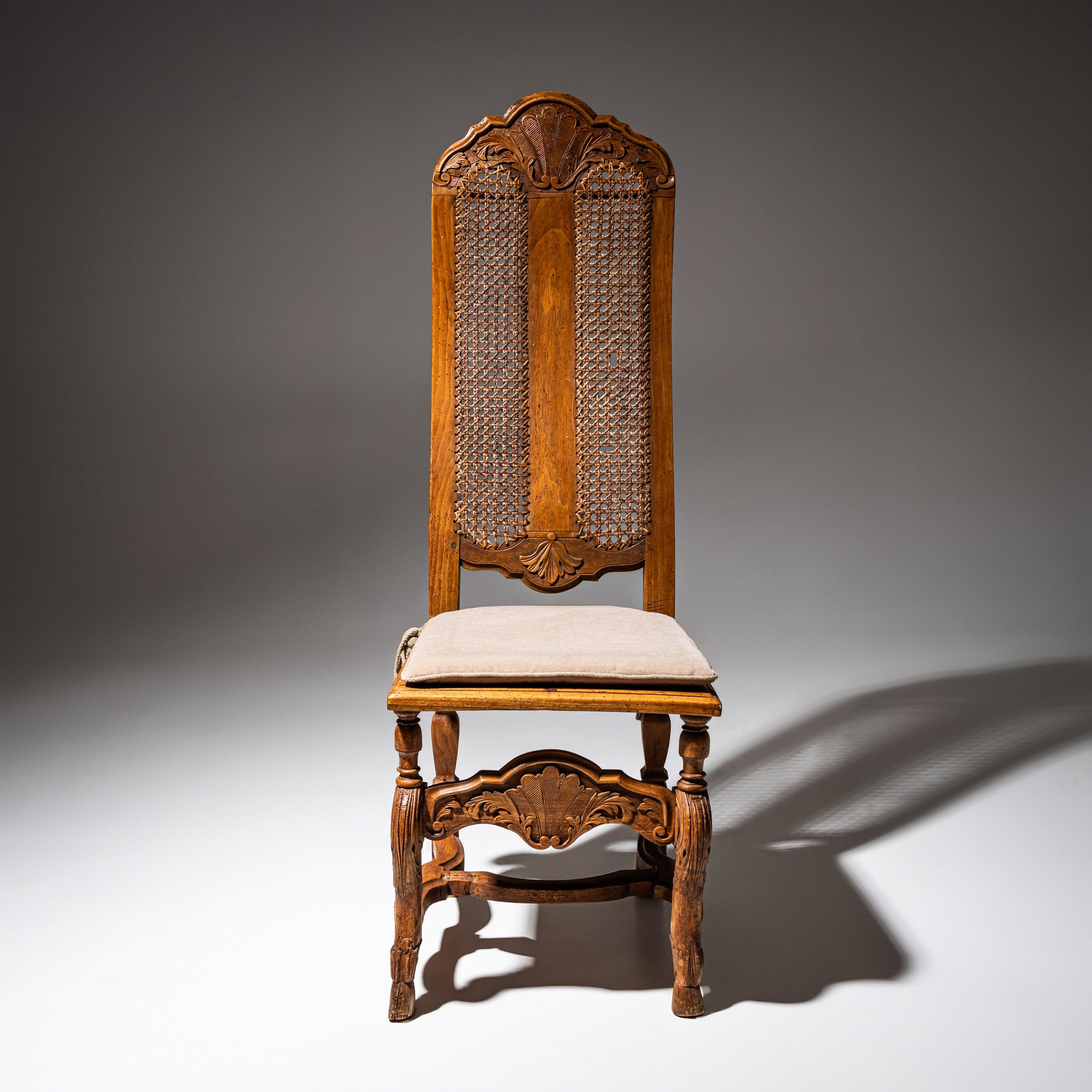 Silla barroca de nogal con respaldo alto de caña. La parte posterior y el marco están decorados con motivos foliados tallados. En perfecto estado.