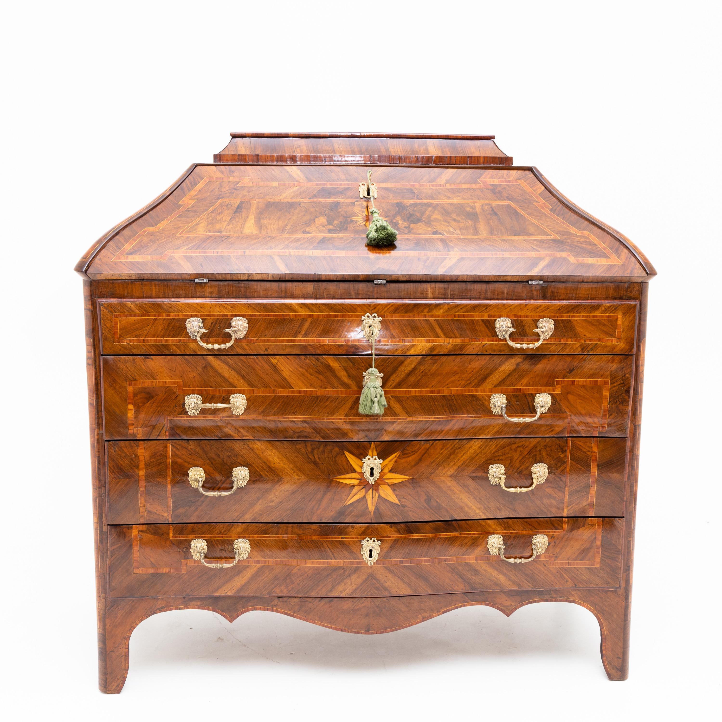 Italian secretaire standing on bracket feet with four drawers and trapezoidal top with an inclined flap. The walnut veneer is contrasted with panel-shaped frames and decorated with a large star-shaped inlay on the front. Behind the writing flap