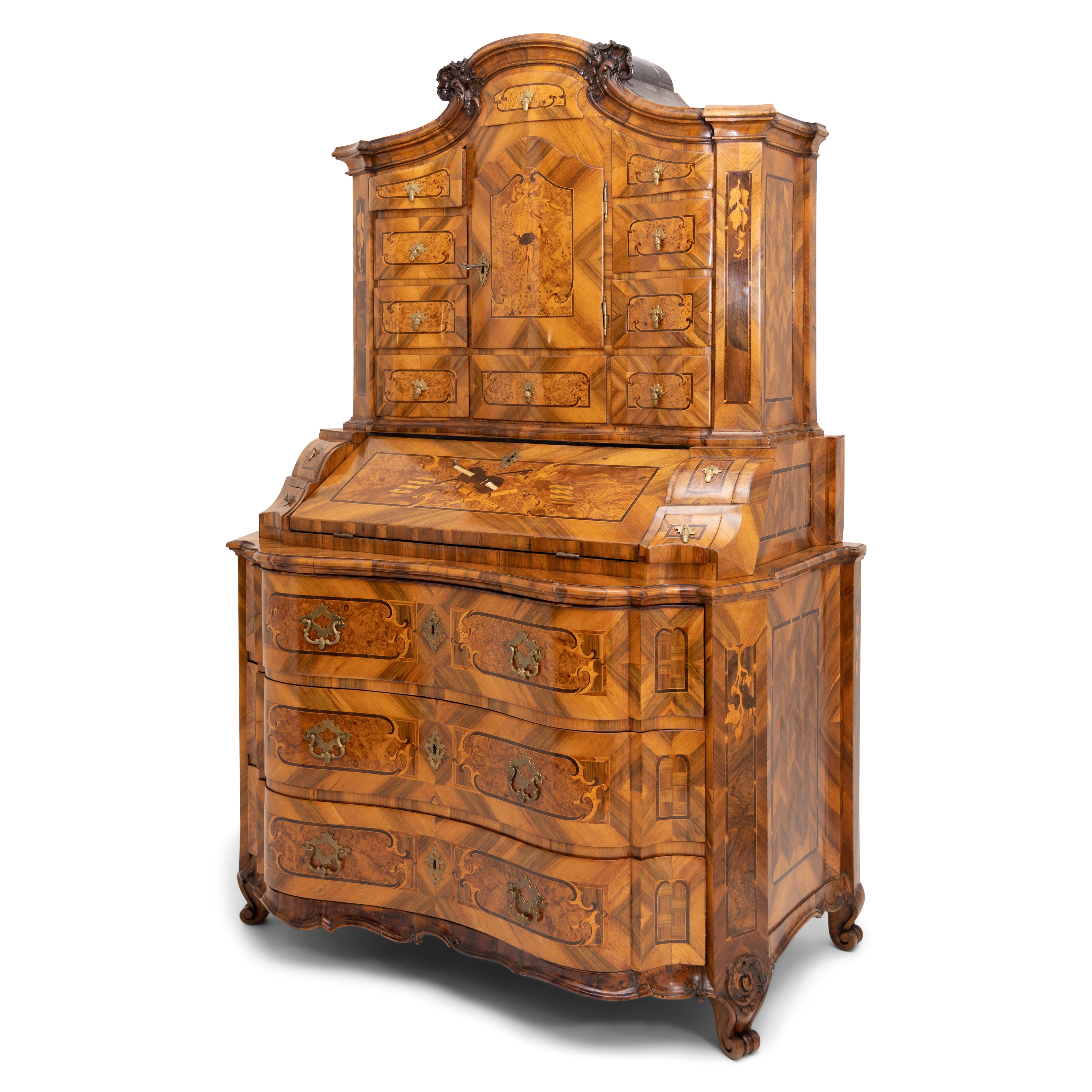 Large Baroque secretaire with a three-drawer chest of drawers in curved form with a wavy skirt. The middle part with a slanted writing flap and four drawers shows a very beautiful marquetry work with violins, flutes and music sheets in different