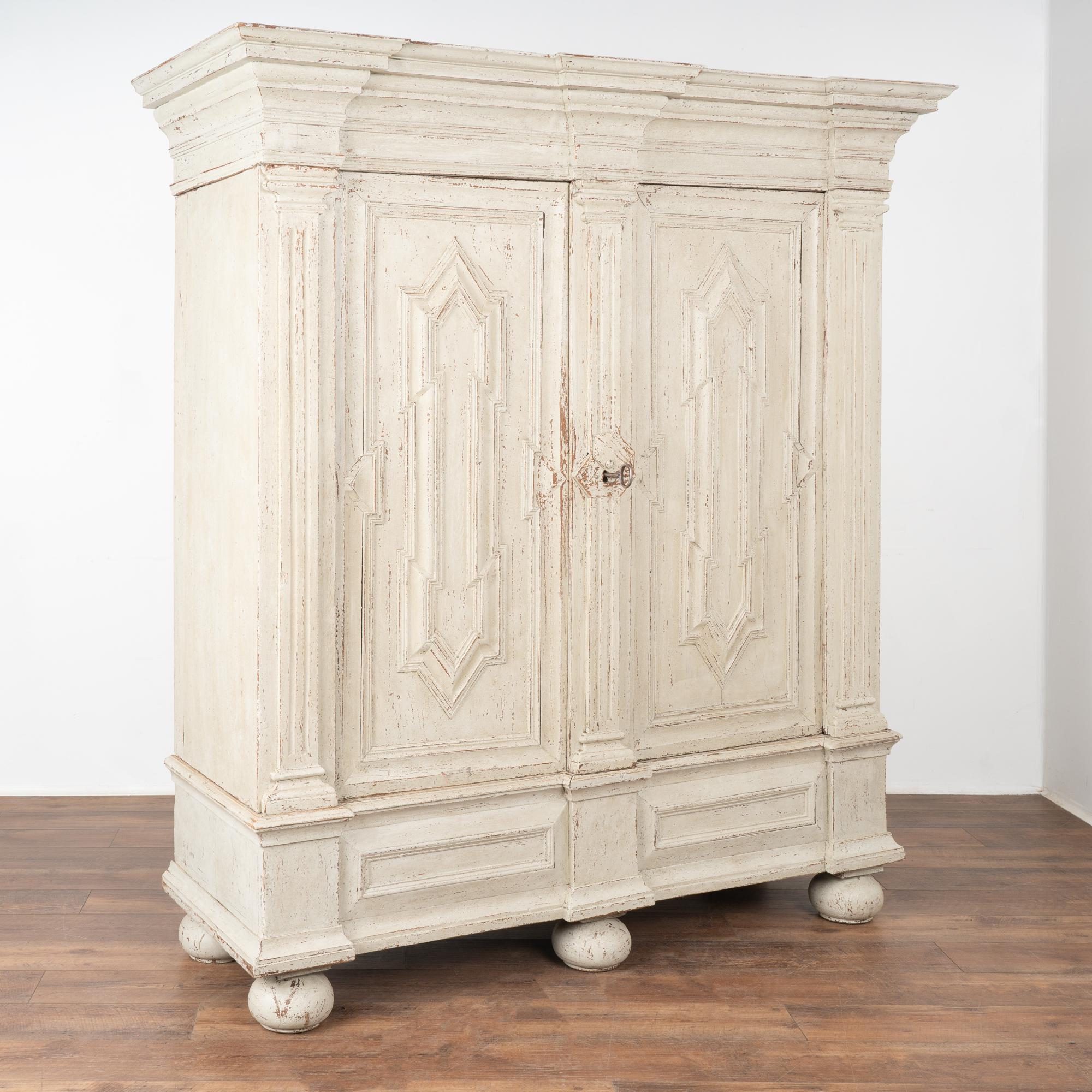 Impressive oak baroque armoire that dates from the late 1700's into early 1800's. Note the heavily paneled doors, massive crown all resting on large bun feet.
Restored, later professionally painted in layered shades of antique white and light gray;
