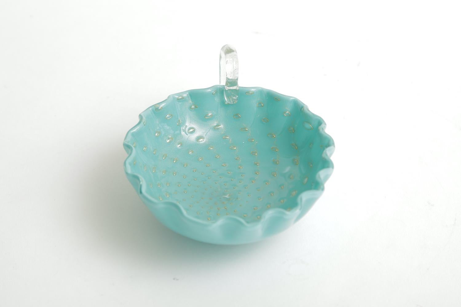 This gorgeous small Italian Murano glass bowl by Barovier e Toso has cinched ruffled edges with a clear glass handle. The color of turquoise offset by the gold aventurine floating in almond shaped droplets with texture is a beautiful combination.