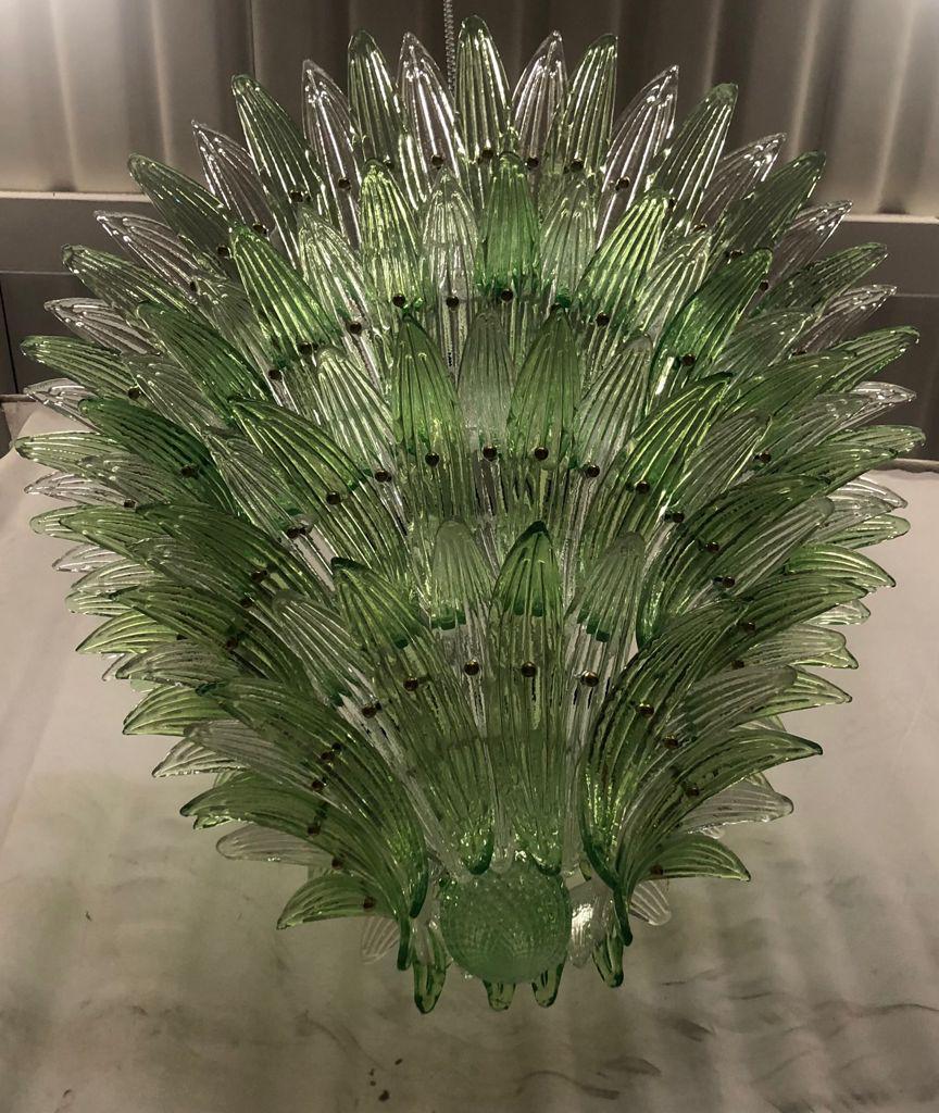 This spectacular chandelier features more than 150 hand made glass palmettes. It has got 4 tiers and a top one. Each glass palmette is fixed with a brass stud. Glass palmettes are all textured and show different nuances of green. Half of them are