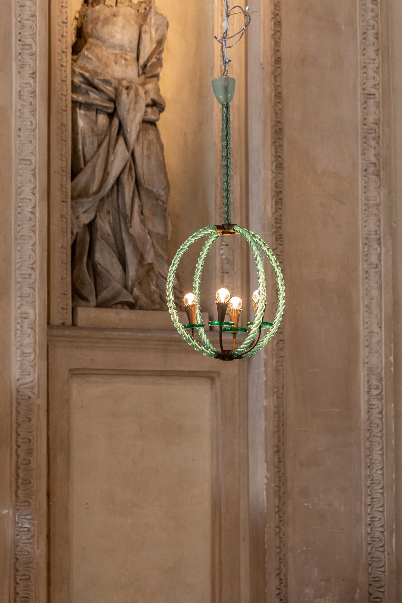 Charming hand blown Murano glass chandelier in the tones of green, with brass details. The structure is composed by two crossing circle elements and four lights.