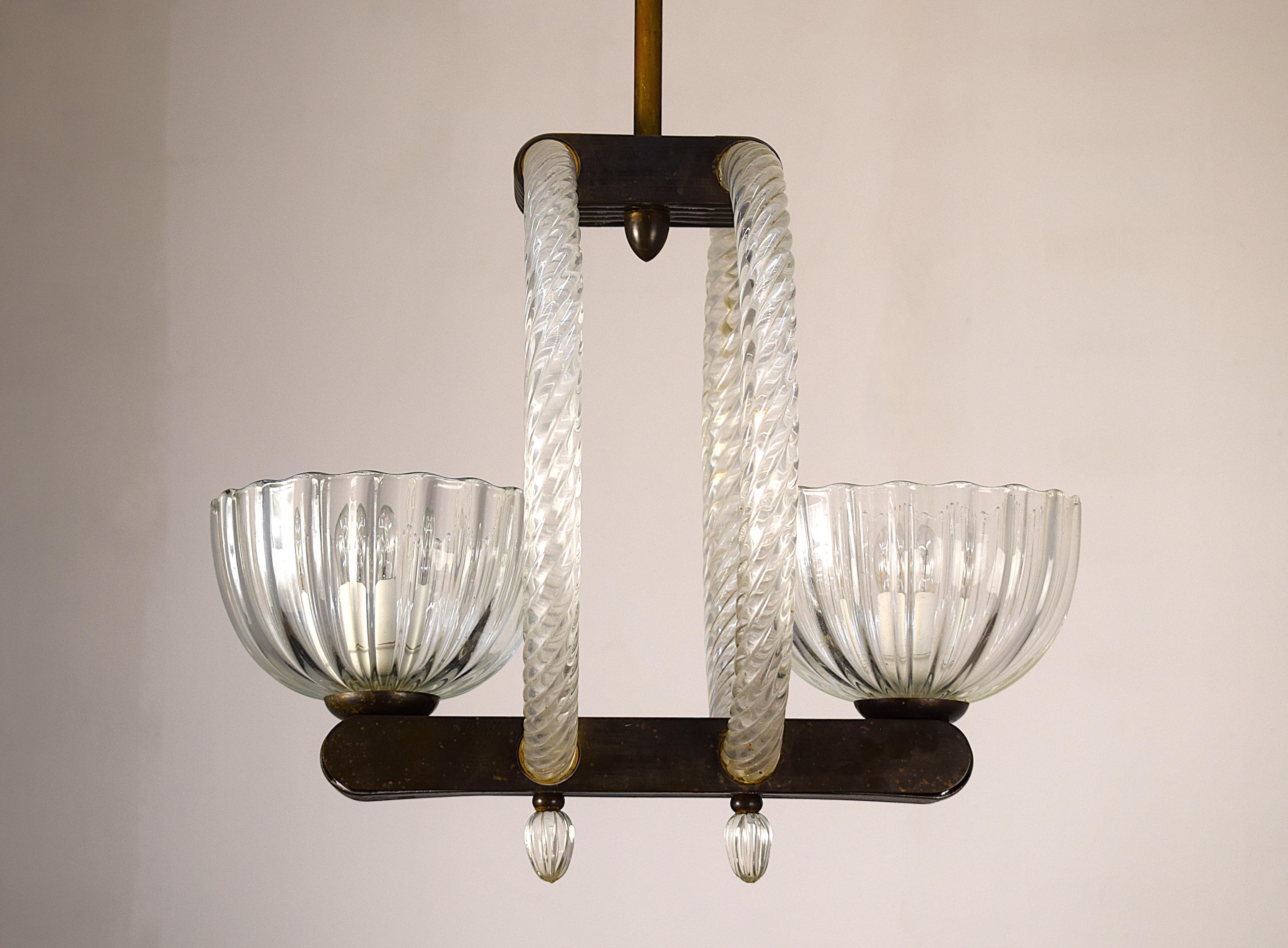 Lampadario Barovier a due luci degli anni ’40, realizzato in Italia in vetro di Murano e ottone. Elegante struttura con linee sinuose e coppe in vetro trasparente lavorato. Misure: 128 cm (altezza), 45 cm (larghezza), 37 cm (profondità). In buono
