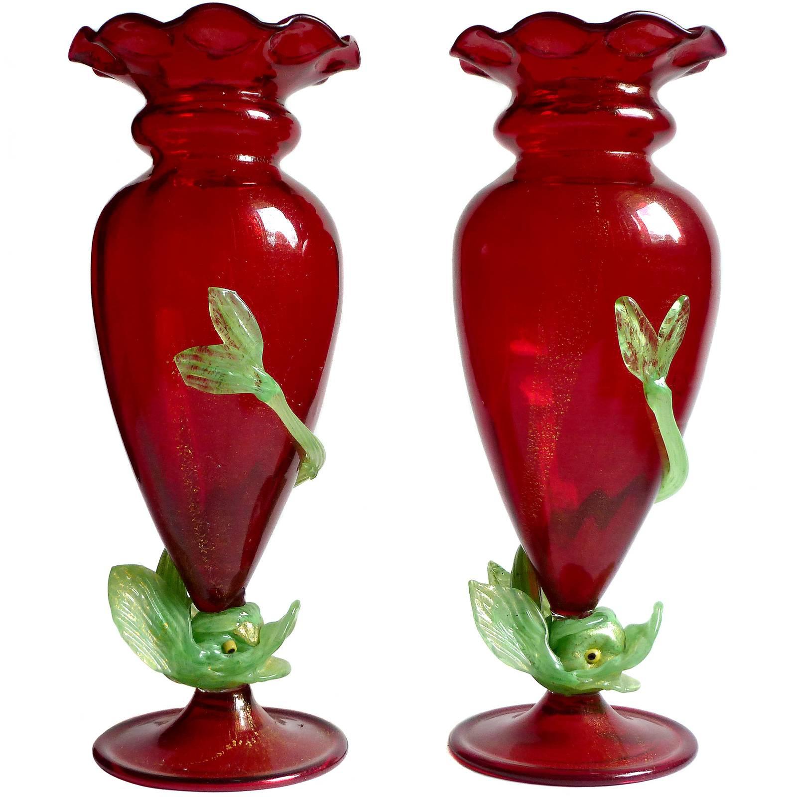 Prezzo per vaso (2 vasi disponibili come mostrato). 
Raro e bellissimo, antico vaso in vetro artistico italiano di Murano soffiato a mano in rosso rubino e macchie d'oro con pesce verde applicato, nello stile dei primi vetri veneziani. Documentato
