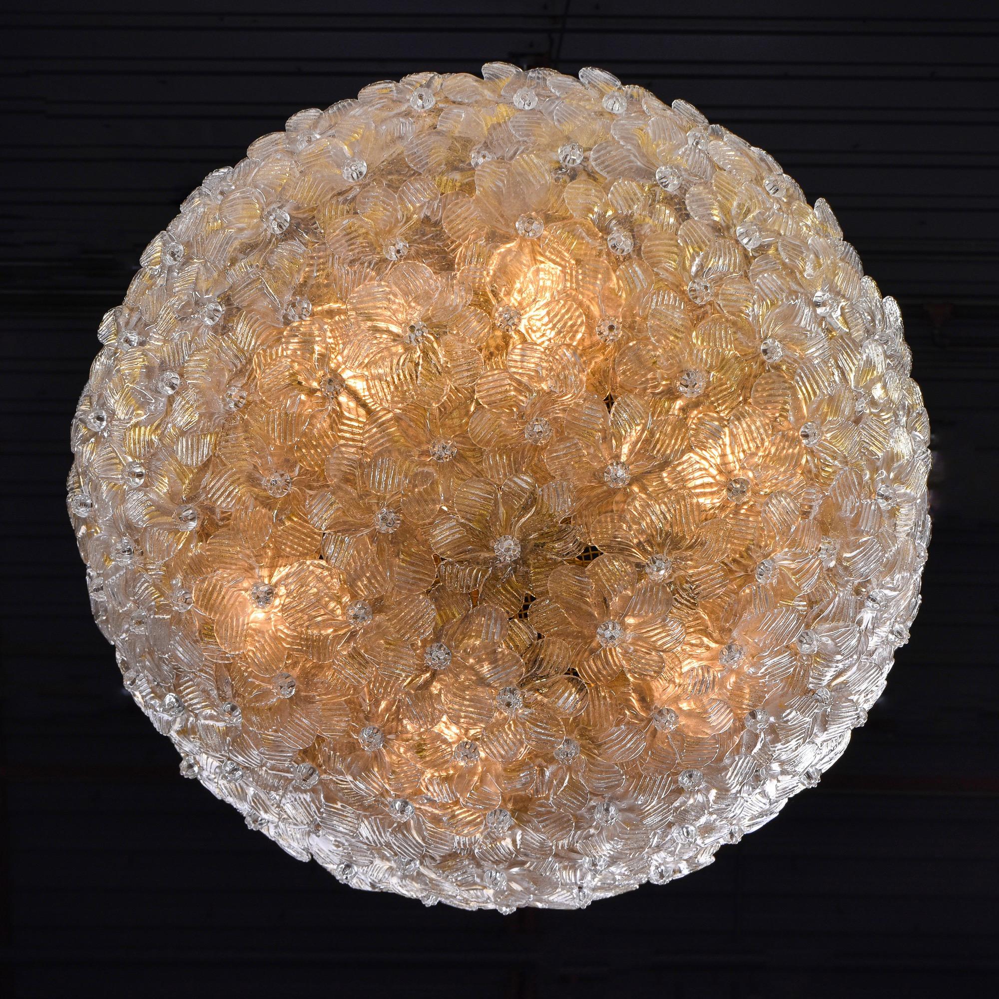 Found in Italy, this circa 1970 semi flush mount fixture is attributed to Barovier. This dome-shaped fixture consists of dozens of clear and gold Murano glass flowers that cover a brass mesh cover. Inside are 6 candelabra sized sockets. Brass