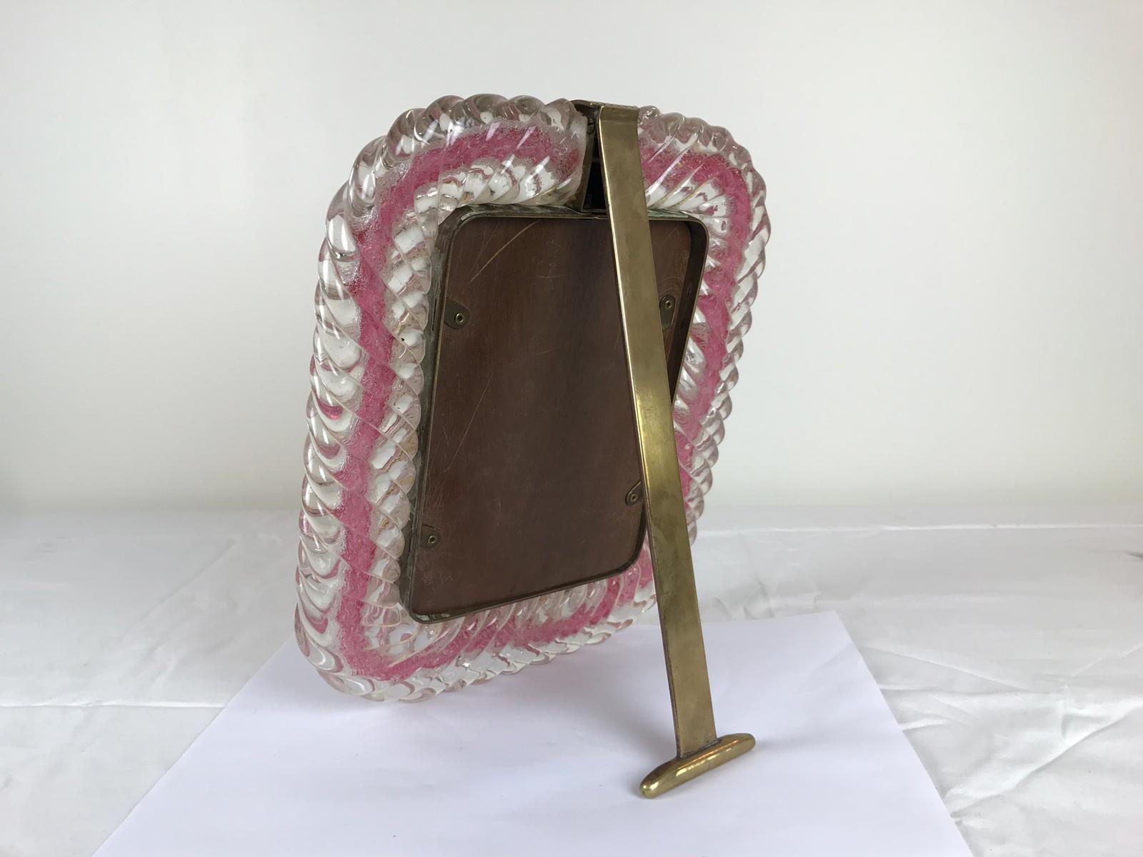 A stunning and rare photograph frame by Barovier & Toso made by Murano with thick hand blown clear glass with and inset ribbon in pink glass and a brass surround and Stand. It has a wooden back.