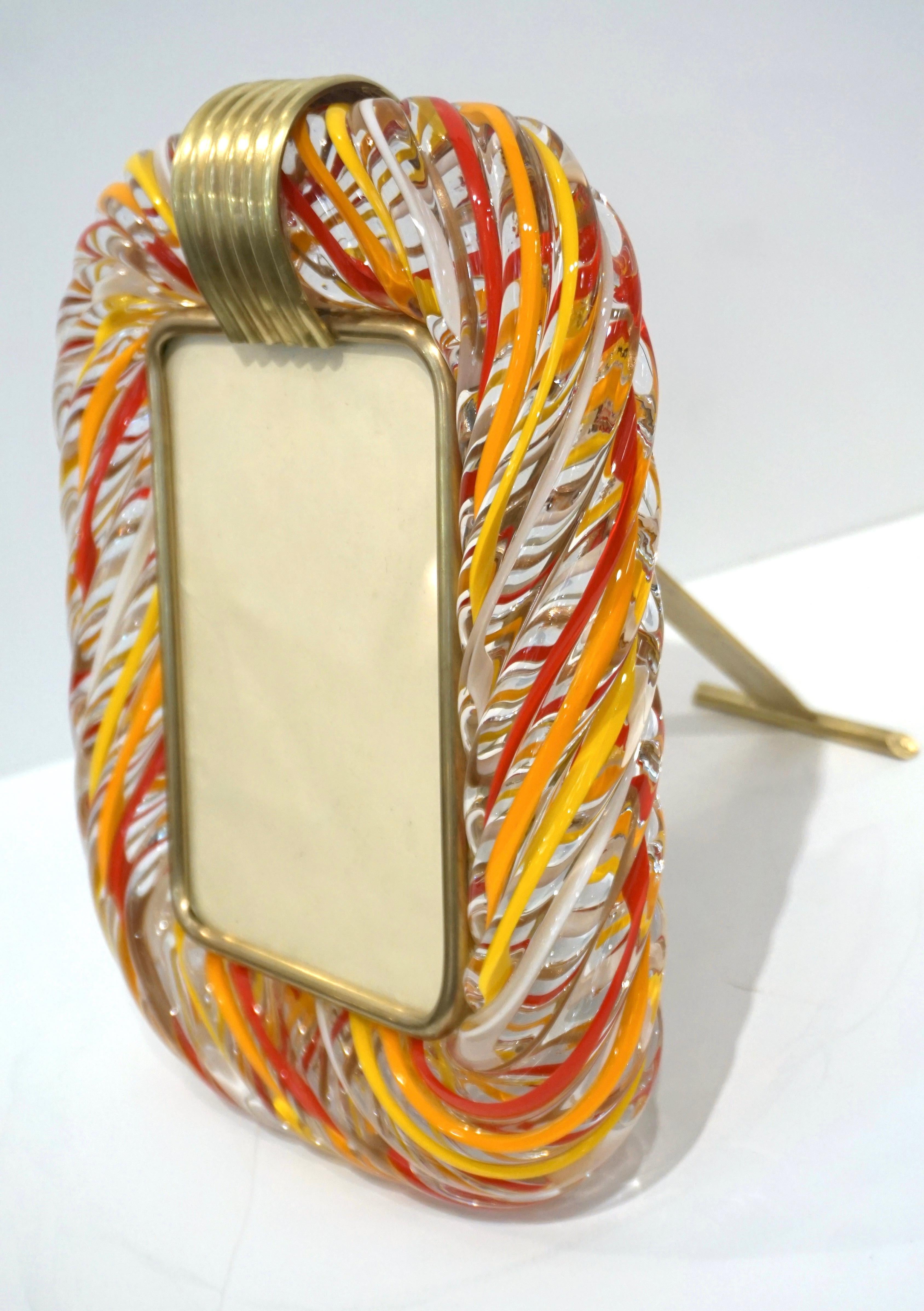 A 1970s modern design Venetian picture frame in thick blown Murano glass by Venini, signed piece, in warm shades. The decoration of the highest quality, with the incalmo of waved coral red, bright orange, mustard yellow and white filigrana inside