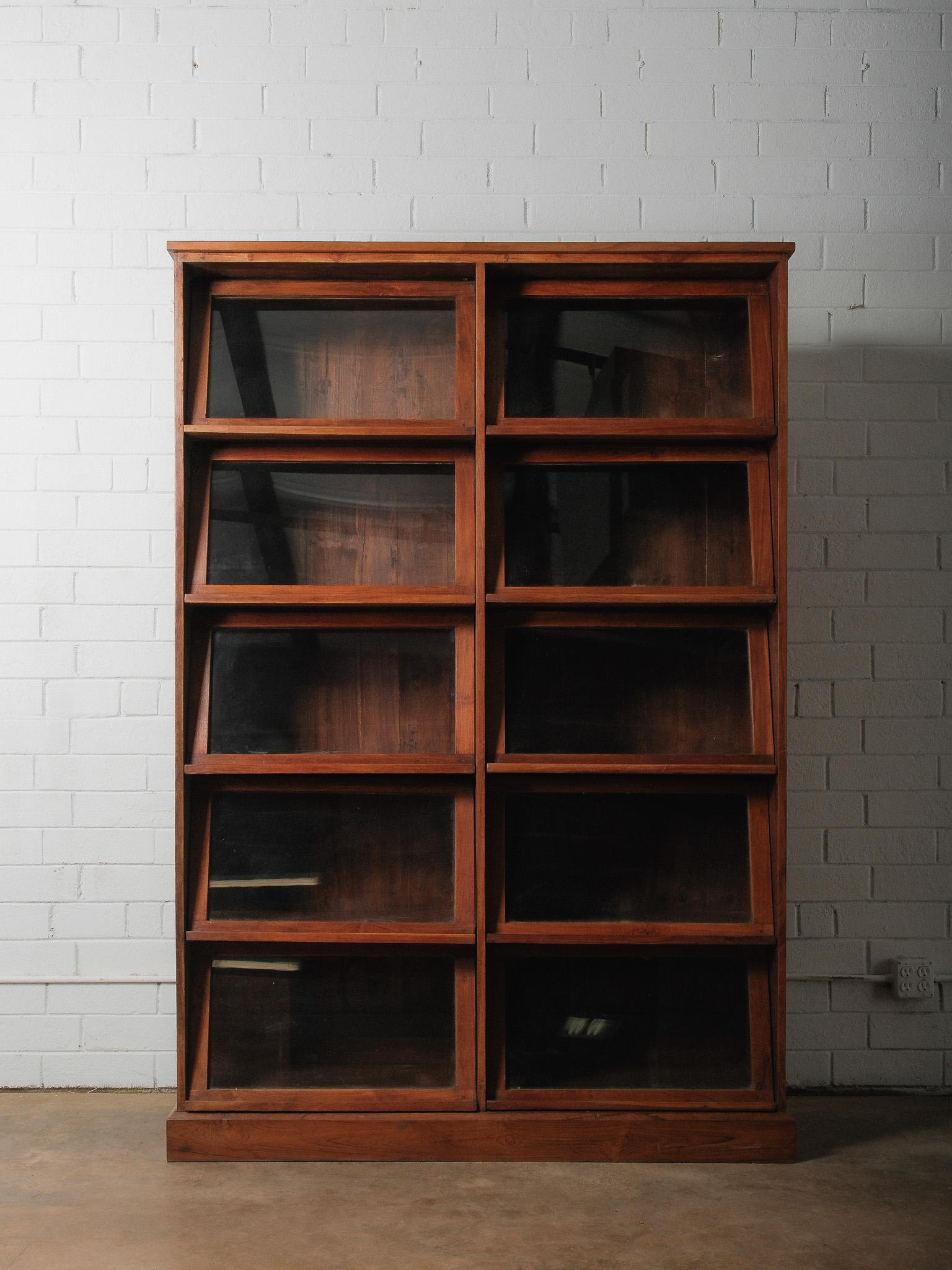 Un grand meuble en bois équipé de portes vitrées disposées en série verticale. La structure est composée de lignes droites et épurées, chaque compartiment étant encadré par des supports angulaires qui donnent de la profondeur à la façade. Les