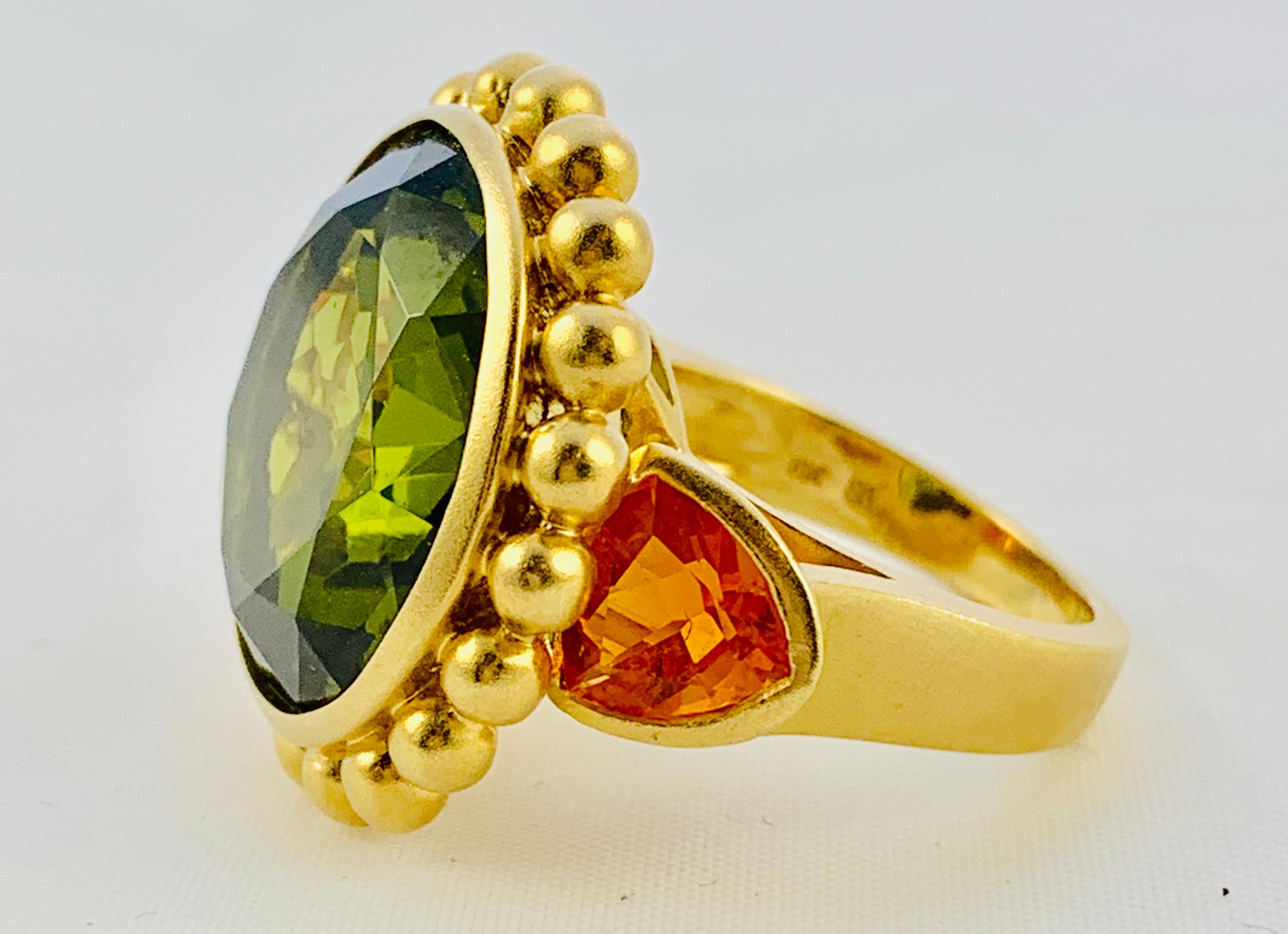 This Ring is an absolute show stopper! Designed by Barry Brinker, it is made in 18K yellow Gold and features a Single, Round, 18mm Peridot that is flanked by two, 7.3mm Orange Sapphires! The retail price on this ring is $7000. It weighs 20.5 grams