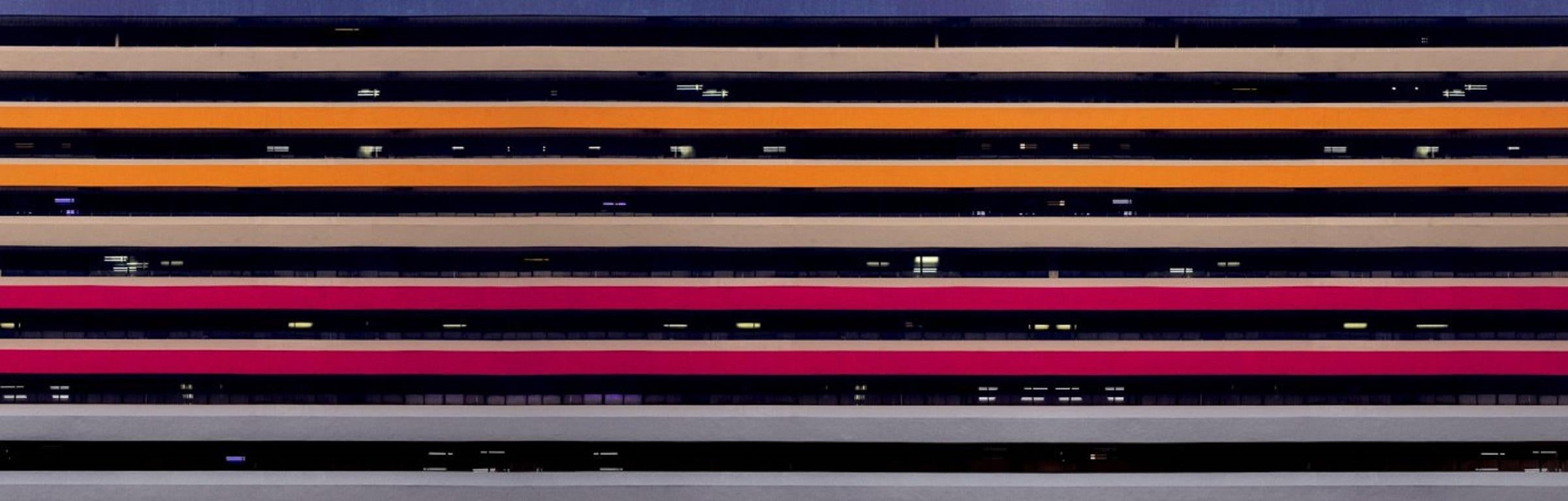 Strips of colour of a multi-storey car park, enhanced by the rain, in Singapore
–
Cawston’s Concrete Jungle is not a vision of the ultramodern, of orderly skyscrapers with comfortable interiors.  It is rather of a Blade Runneresque postmodern world