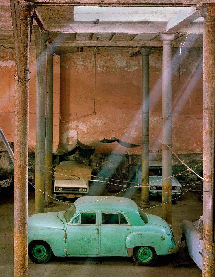 Streams of light illuminate a dilapidated Cuban car in a dilapidated  building in Havana
–
The Spaces in Between series developed out of visits to Naples in Italy and Havana in Cuba, two cities whose past glories are suffused with a faded grandeur. 