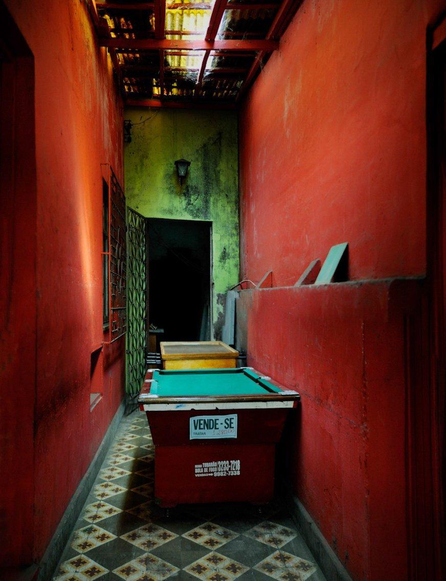 The green baize of an old pool table awaiting a buyer  amidst the deep red of a storeroom.
–
The Spaces in Between series developed out of visits to Naples in Italy and Havana in Cuba, two cities whose past glories are suffused with a faded