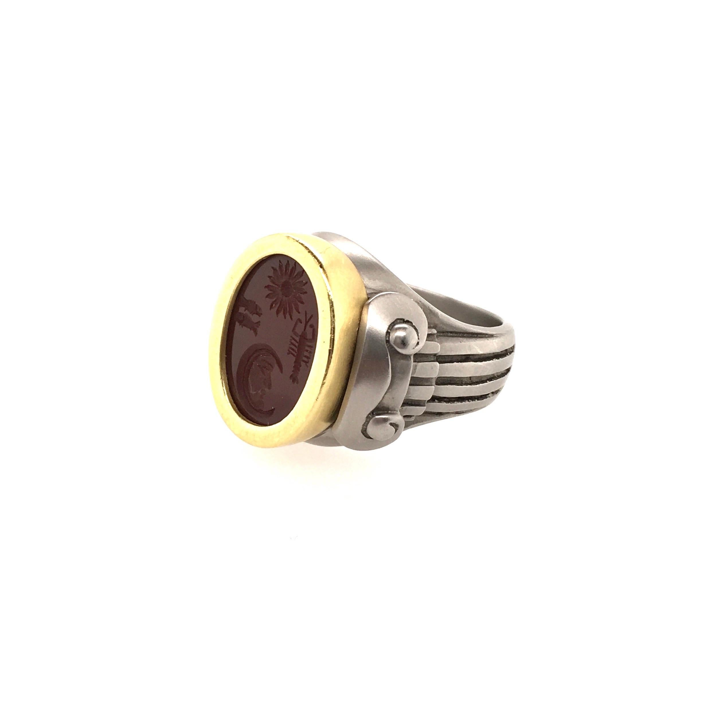 A stainless steel, 18 karat yellow gold and carnelian intaglio ring. Barry Kieselstein Cord. 2000. Designed as a stainless steel ring with column shoulders, centering an oval carnelian intaglio carved with sun, moon, fish and lobster motifs, within