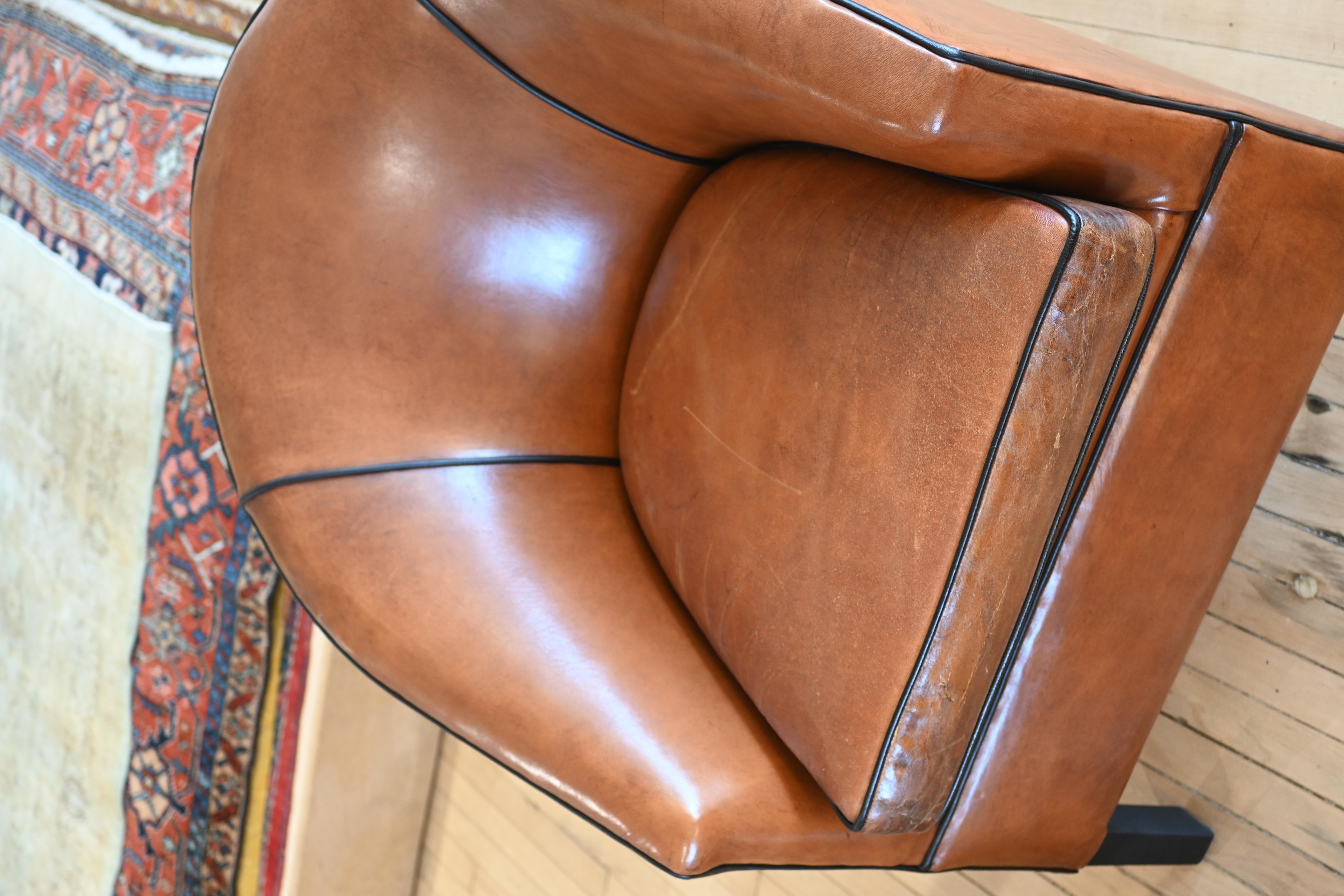 Un magnífico sillón club de cuero holandés, obra de Bart Van Bekhoven. Patas delanteras cónicas de cuero y una exclusiva pata de cuña como soporte trasero. Bonito tono del cuero con detalles de ribetes negros y un desgaste increíble. 