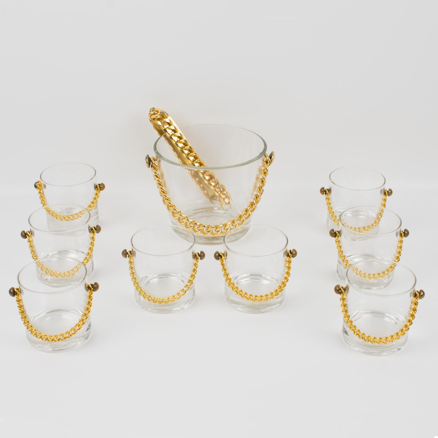 This stunning modern barware cocktail set features an ice bucket with eight matching whiskey glasses and dates from the 1980s. The incredible chic shape boasts a gilded metal chain decor on each piece. The ice bucket has a glass body with a gilded