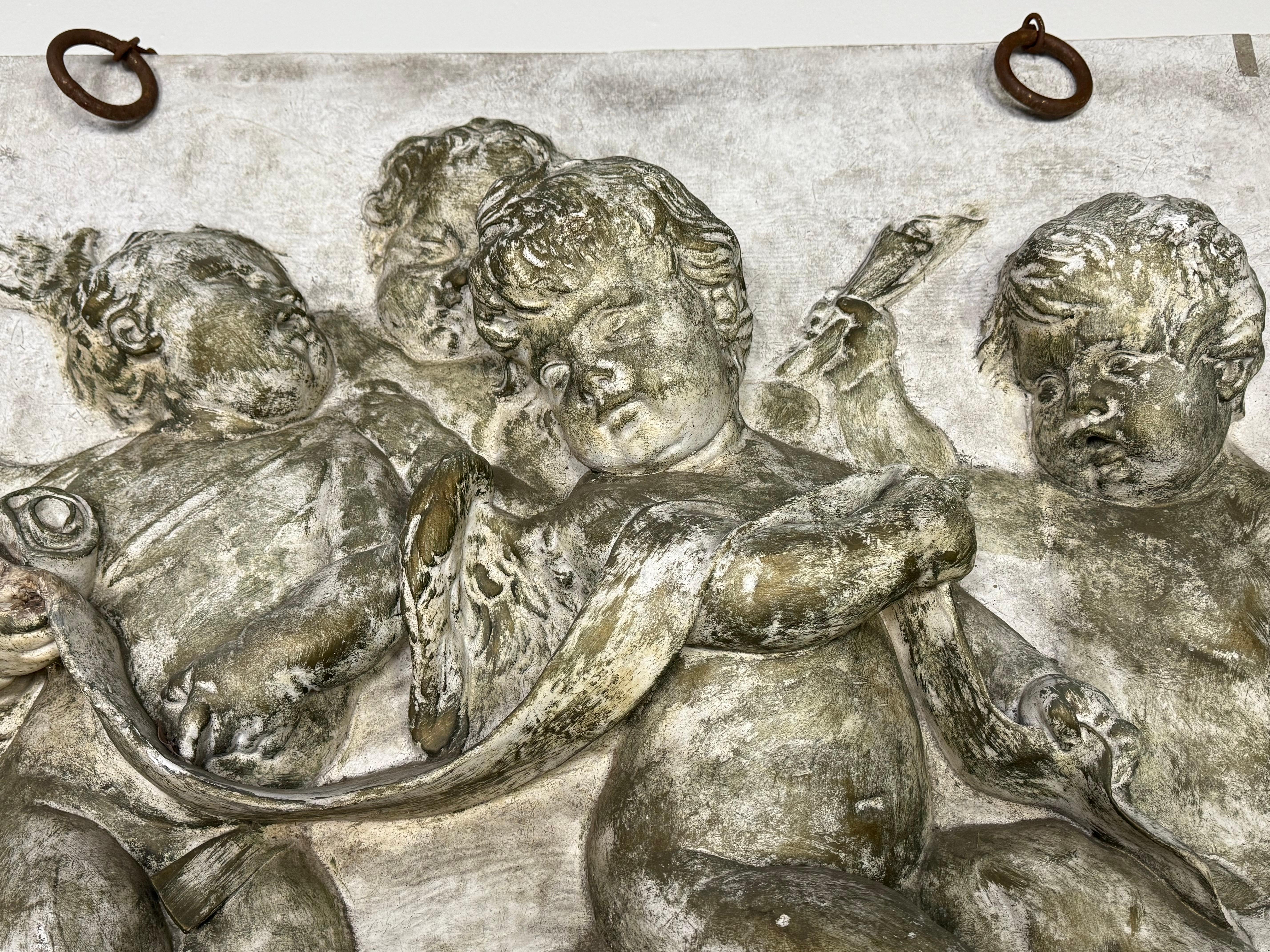 Tenture murale représentant un bas-relief avec des figures de chérubins, inspiré de l'art de la Renaissance.  Le relief est fait de plâtre et de crin de cheval et présente une patine vieillie.

La scène se compose de quatre chérubins, qui