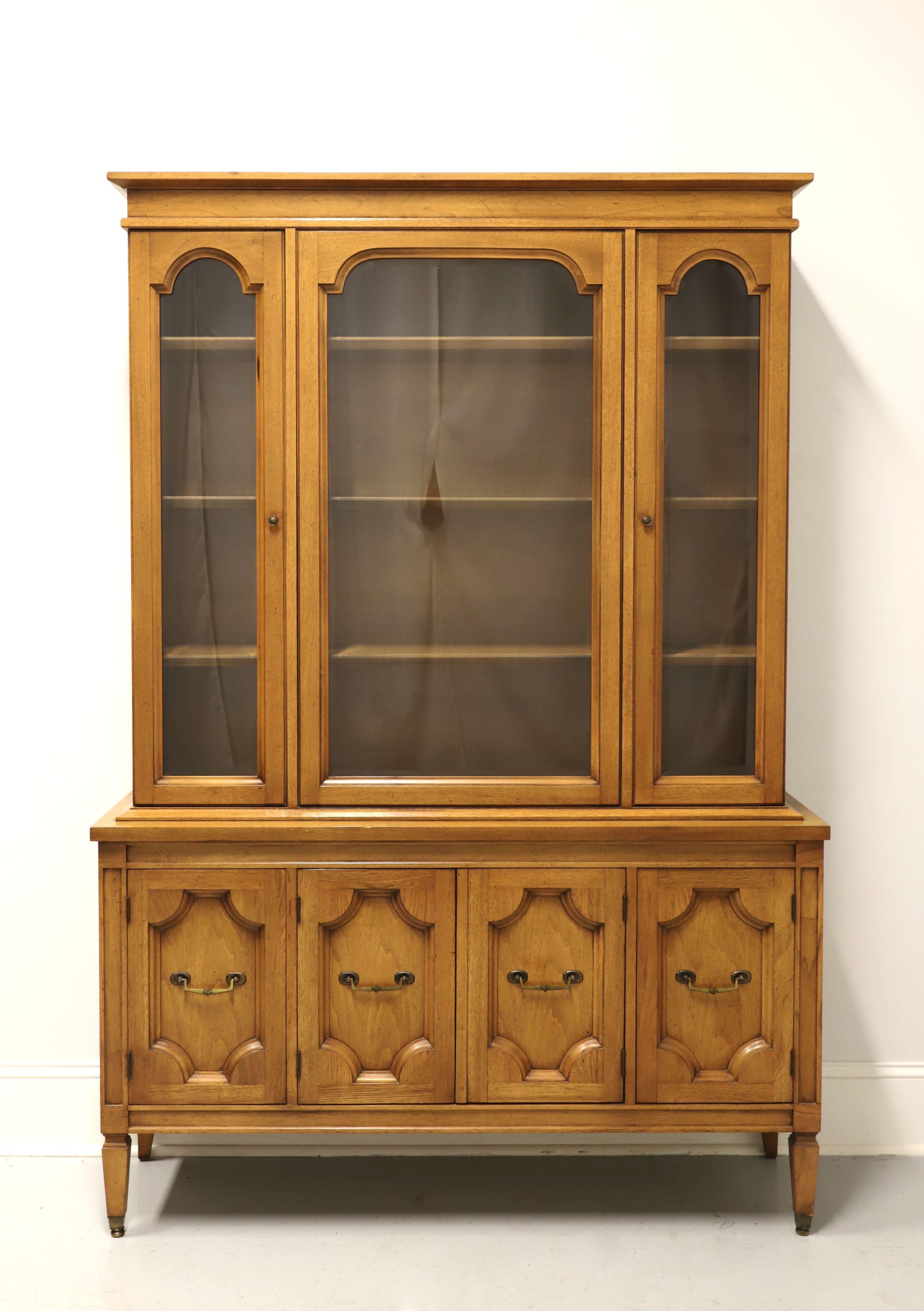 A mid 20th century Mediterranean style china cabinet by Basic Witz. Pecan, or similar nutwood, with brass hardware, crown molding to top, carved lower cabinet doors and spade feet. Upper cabinet features three fixed plate grooved wood shelves behind