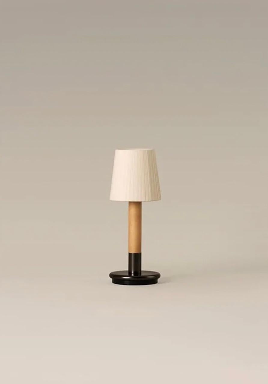 Básica Mínima Batería is the portable version of Básica Mínima. Its cylindric structure, made of birch wood, holds two lampshade options: pleated natural parchment and ribbon stitched. With a light touch, the lamp turns on and off, making it a light