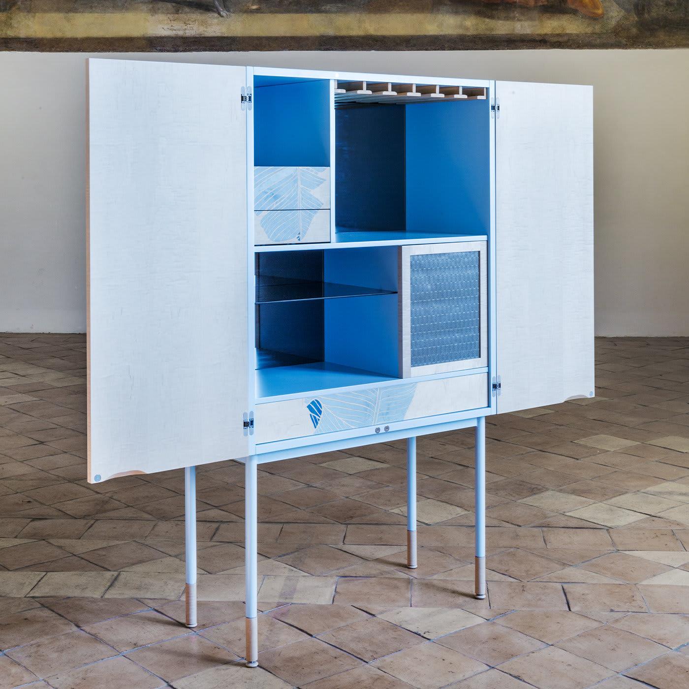 Marked by a delightful white and azure color palette, this cabinet draws inspiration from the unattainable perfection of nature. It stands on thin metal legs, creating an appealing interplay of solids and voids with the storage unit above, which is