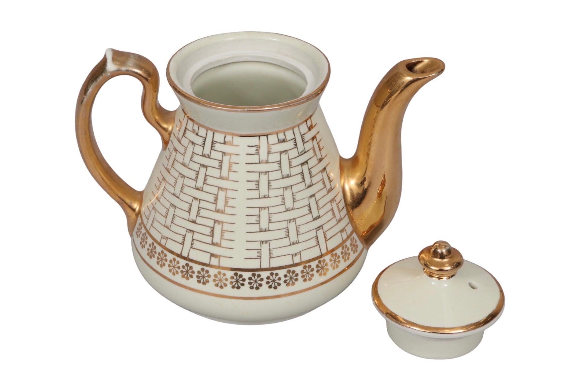 A ceramic teapot by Hall's of Philadelphia. The main body of the teapot is in ivory, whilst the handle, spout and basket weave pattern are in gold. Maker's mark underneath.