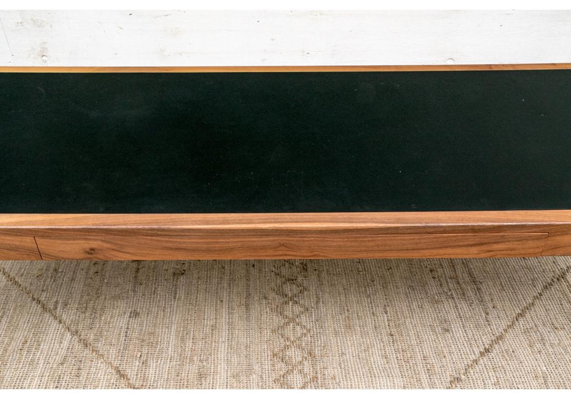 A custom long rectangular table having a slim silhouette with an inset vegetable-tanned black leather top, raised on demilune tapering legs with flat backs. The long flush leather-lined frieze drawer with compartments.
Designed by Craig Bassam &