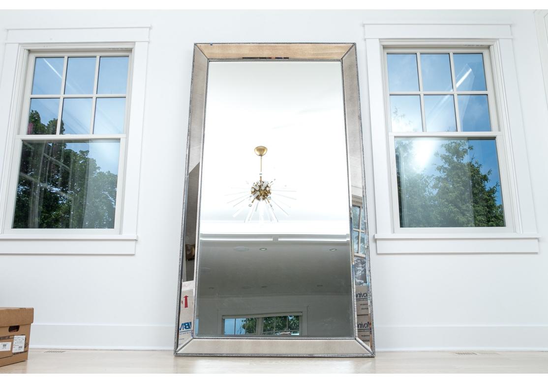  Very large Leaning Mirror by Bassett with fine optical property. The mirror features a wood and beveled antiqued mirror frame with a beaded edge with perimeter beveled mirror glass panels. The mirror is intended to be a floor standing mirror that