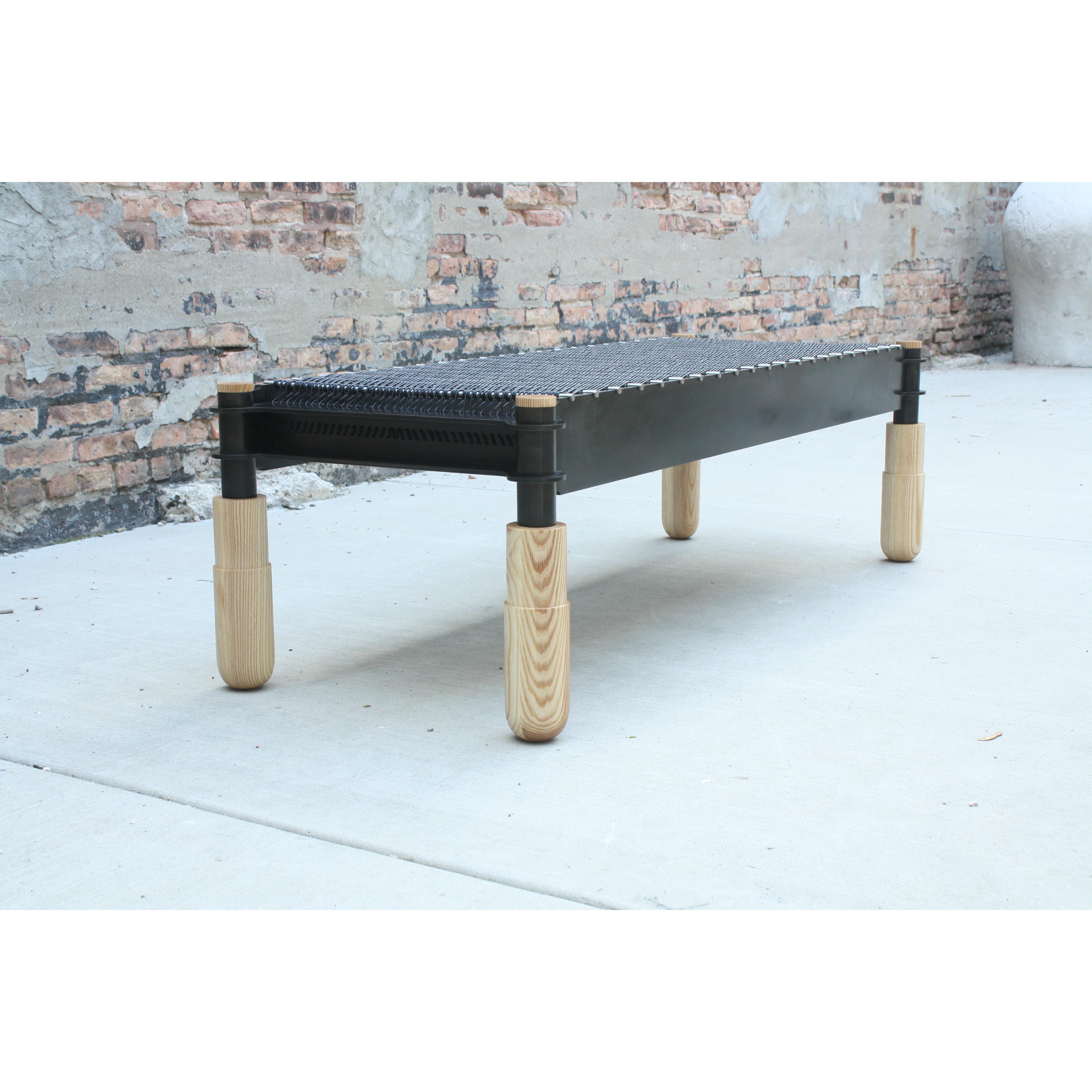 Shown in blackened steel, brushed stainless, oiled ash, and black leather.

This handmade bench features interlocking joinery executed in steel supported by hand-turned solid wood legs. Leather cord is woven through brushed stainless dowels and