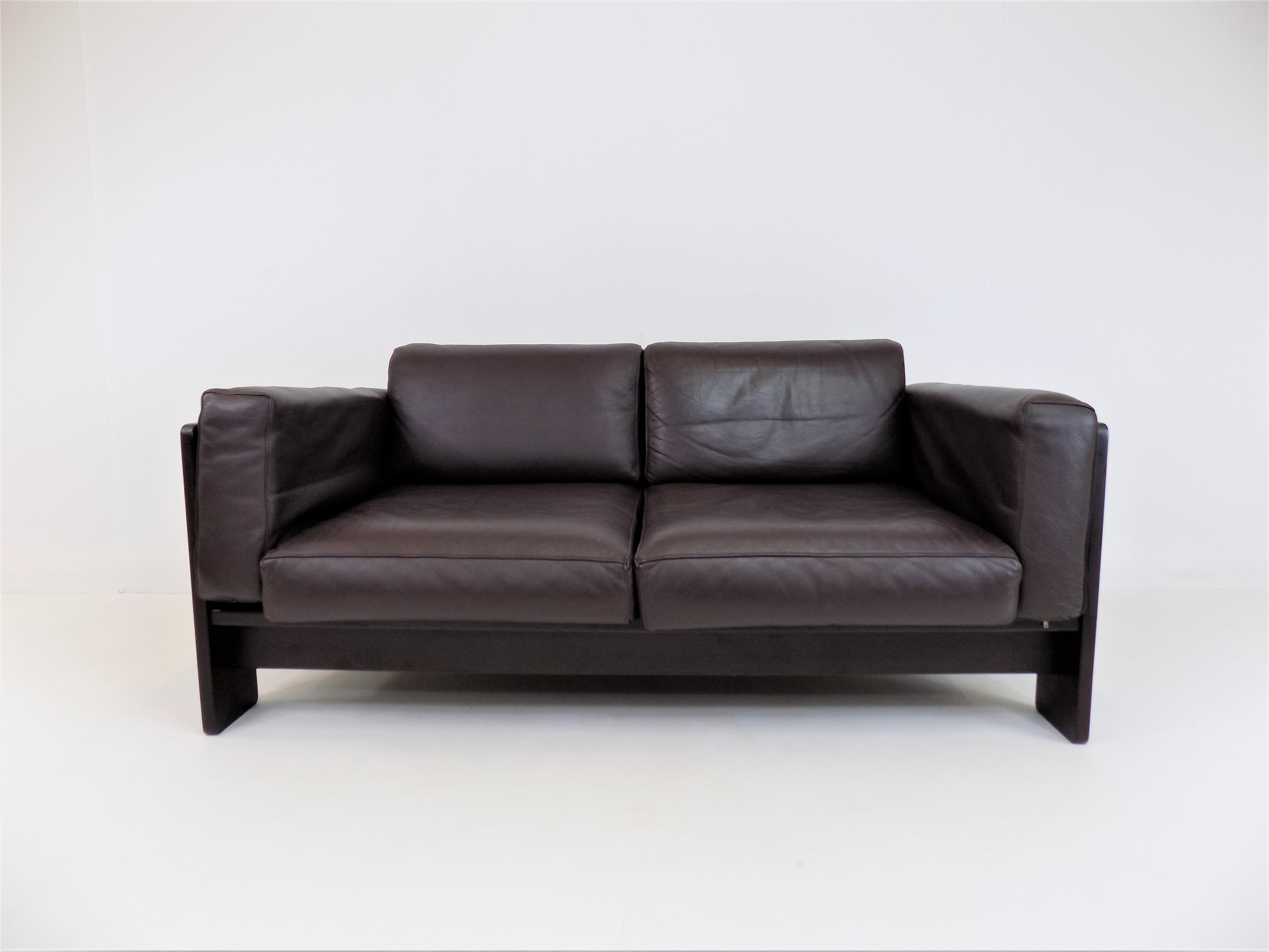 Dieses Zweisitzer-Sofa aus dunkelbraunem Holz und braunem Leder ist in ausgezeichnetem Zustand. Der fast schwarze Holzrahmen harmoniert sehr schön mit dem etwas helleren Braunton des Leders. Das weiche Leder ist in fast neuem Zustand, der Holzrahmen
