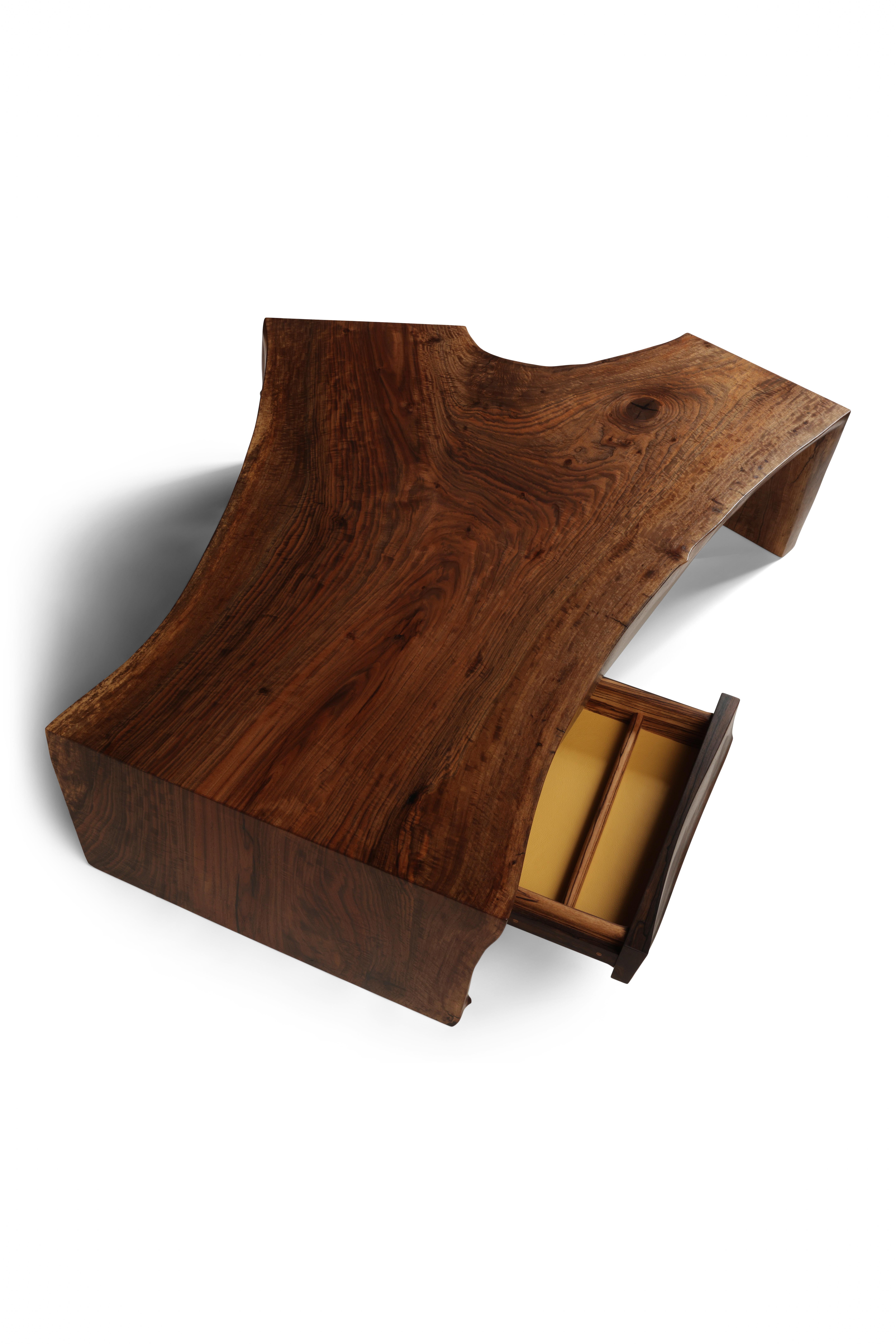 A single slab of figured Bastogne Walnut folded to create a waterfall effect over the ends of the table. An organically sculpted drawer is seamlessly tucked away into one corner.  The drawer front carved in decadent Ziracote accented by a Zebrano