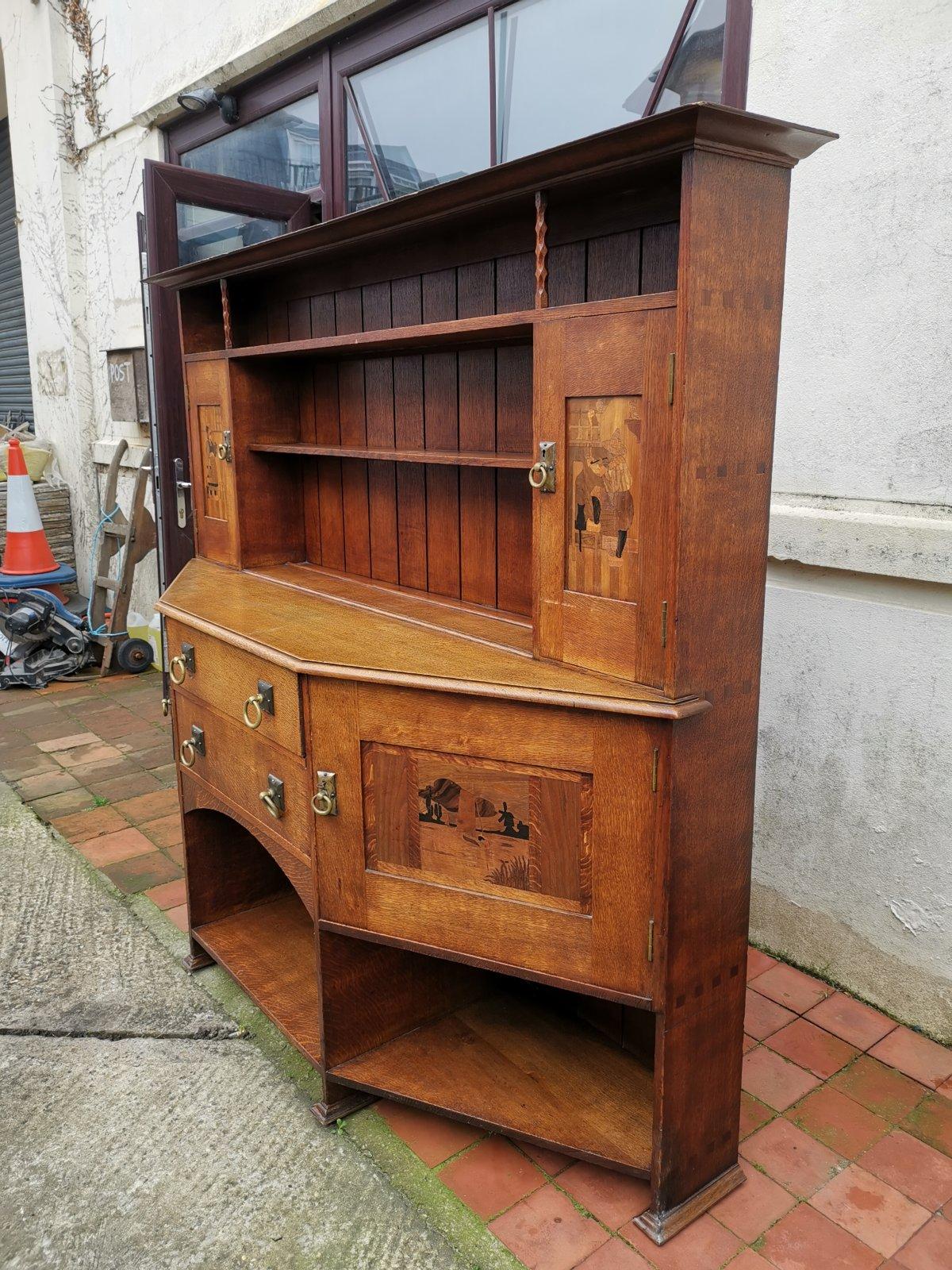 Bath cabinet makers. In the Liberty style.
An early Arts & Crafts oak break front sideboard with Dutch inlaid scenes of mill owners with there little black cat in the two upper cupboard doors, to the lower cupboards on his horse and a sailing