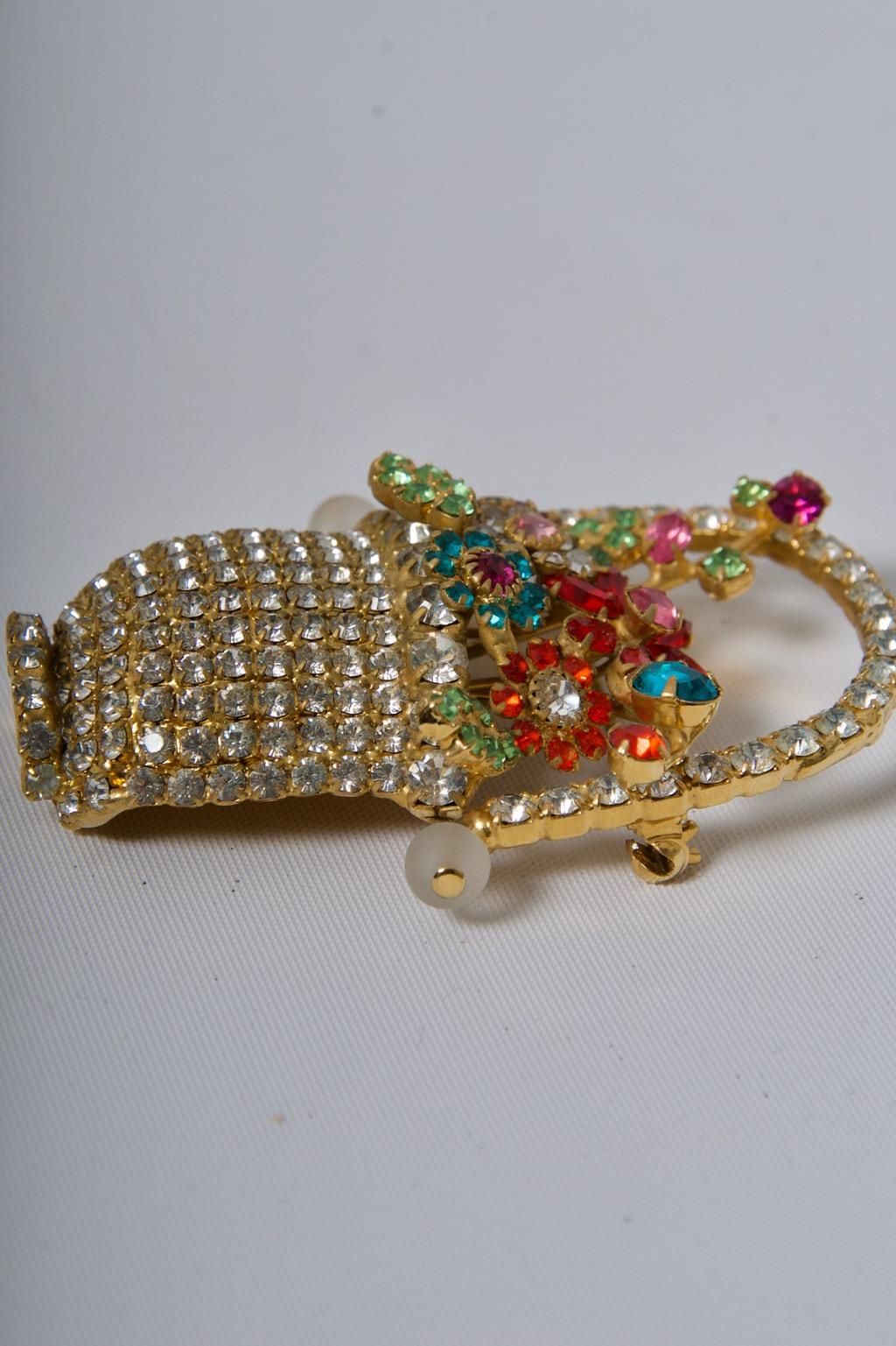 Dorothy Bauer was known for her sculptural, whimsical jewelry designs incorporating Swarovski crystals, as exemplified by this brooch. She was active in Berkeley, CA, from 1982-2008. the brooch replicates a handled flower basket of clear crystals