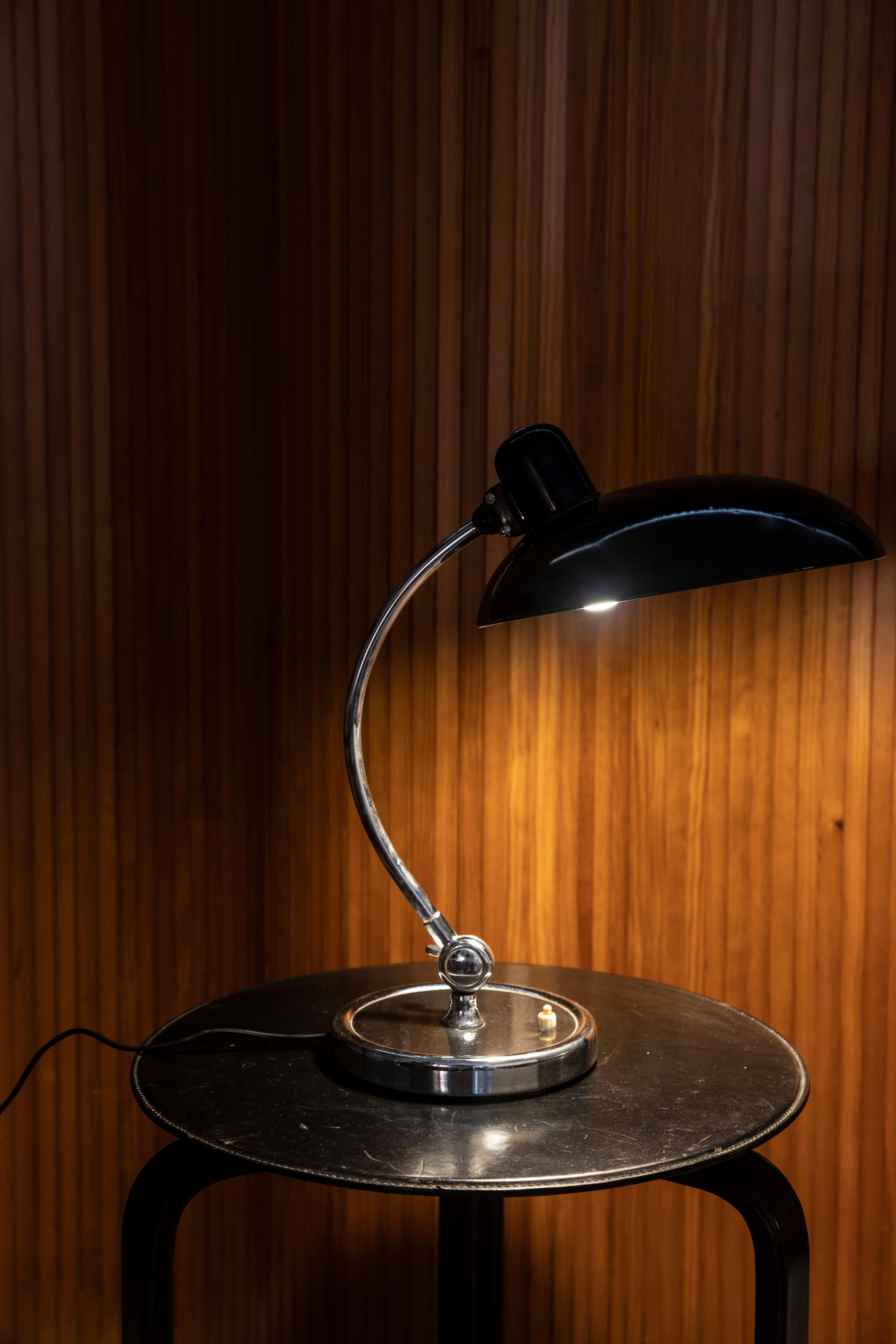 Elegante Schreibtischlampe im Bauhaus-Stil mit einem schwarz emaillierten Metallschirm und einem gebogenen Arm aus verchromtem Stahl auf einem runden, beschwerten Sockel. Seine klare Geometrie und funktionale Konstruktion verkörpern die