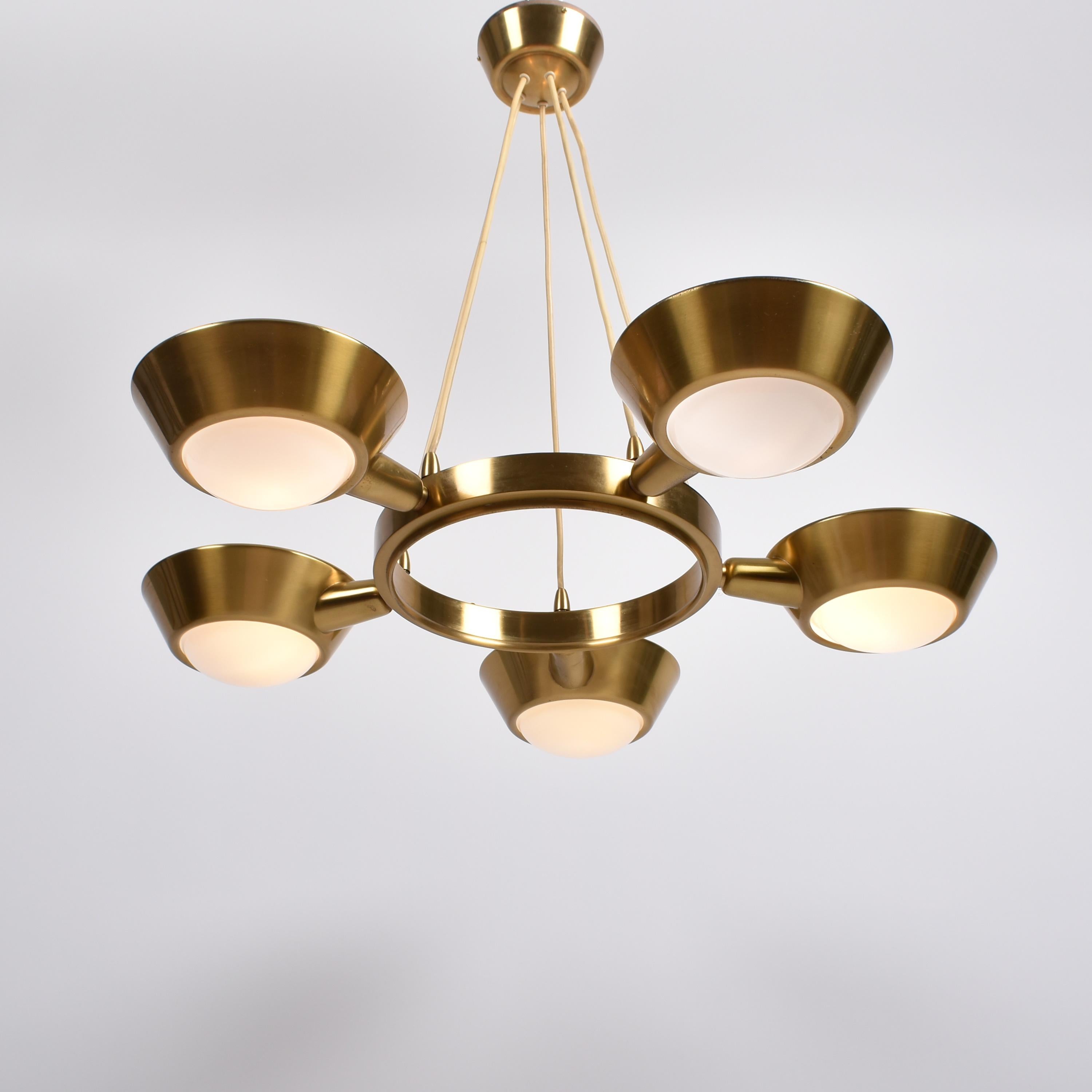 Large brass chandelier with five lights , Switzerland, 1940.
Five reflectors, brass outside and white lacquered inside, are placed around a brass circle.
The reflectors have a frosted glass lens, which indicates an early production (1935 - 1940),