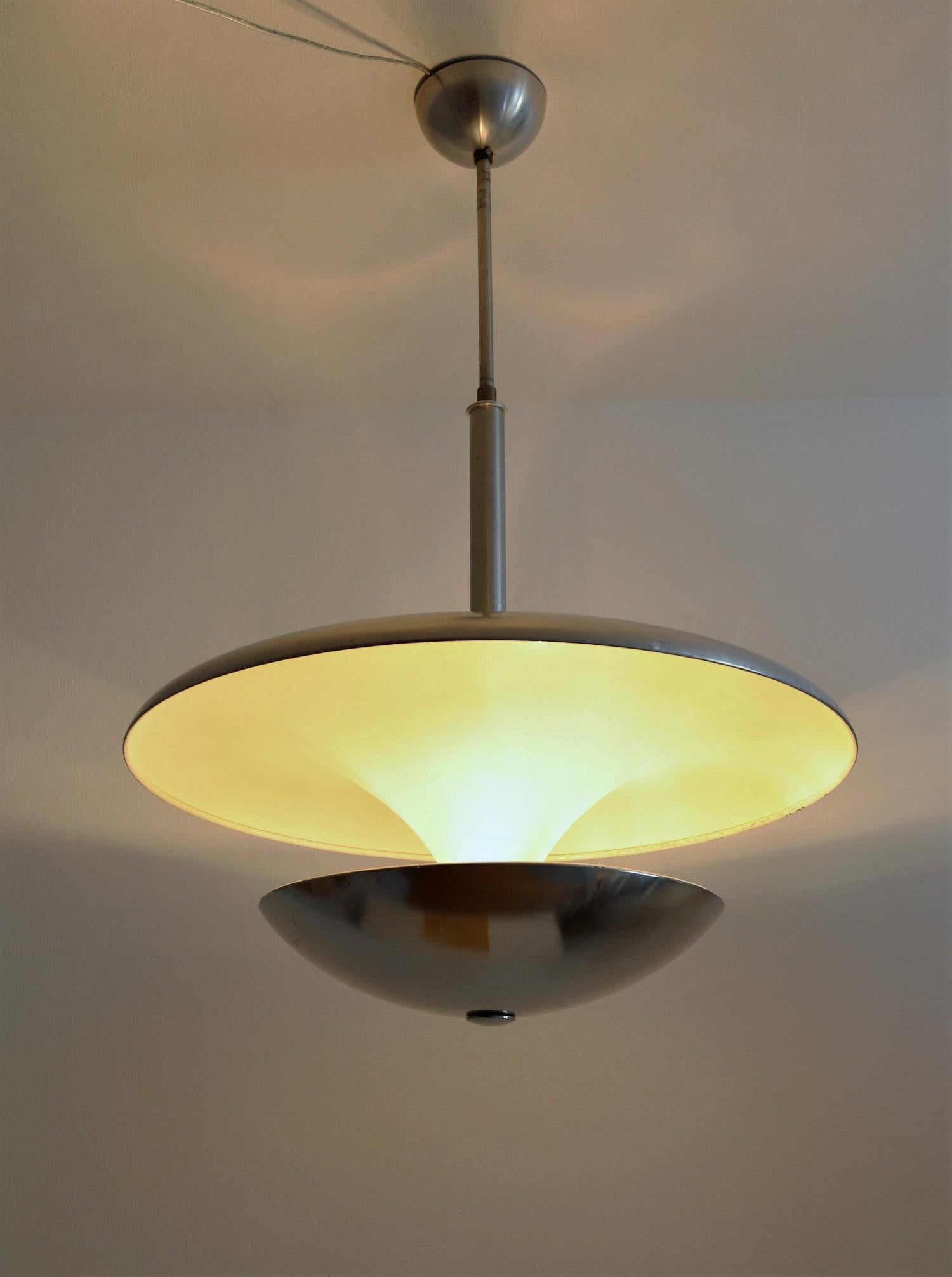 Magnificent chandelier made completely of aluminium during the Bauhaus period.
The upper big plate is down-going in a tulip shape, and on its bottom is fixed a round dome. It's varnished inside in cream white to reflect warm light when illuminated