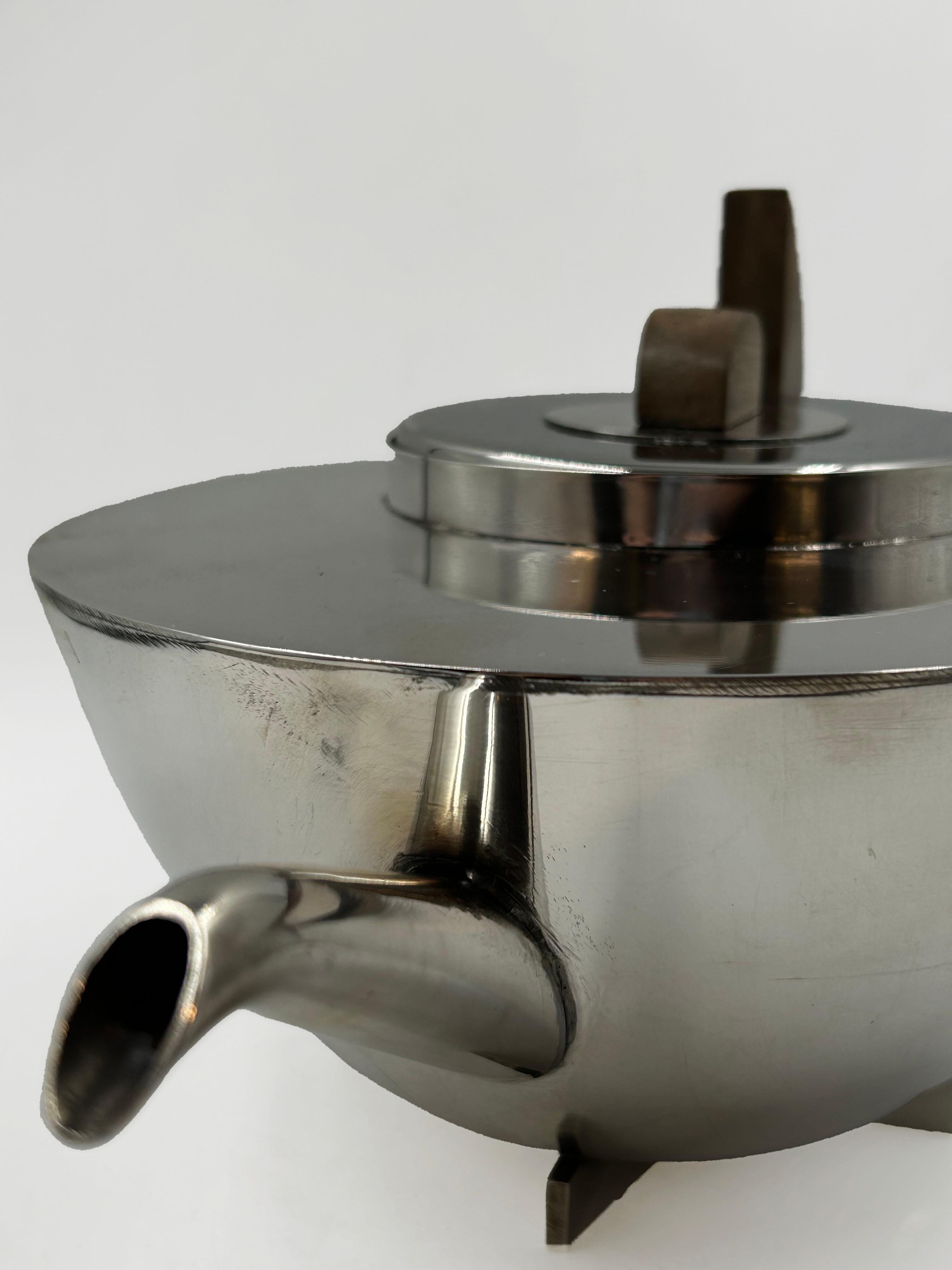 Théière en métal argenté Bauhaus Art Deco
Cette théière présente un design nettement influencé par le Bauhaus, caractérisé par la simplicité géométrique et la fonctionnalité. Le corps est une sphère segmentée en métal argenté ou chromé avec une